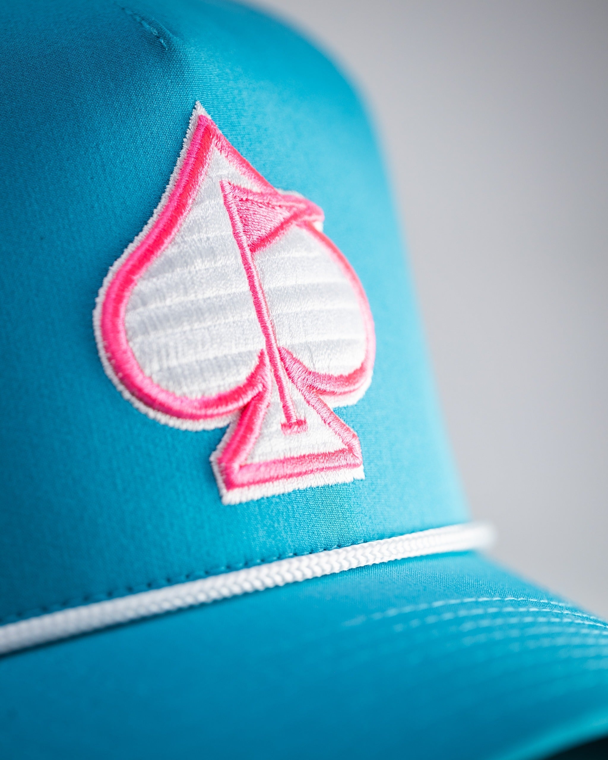 Perforated rope hat in baby blue featuring a pink spade logo, perfect for stylish golfers on the course.