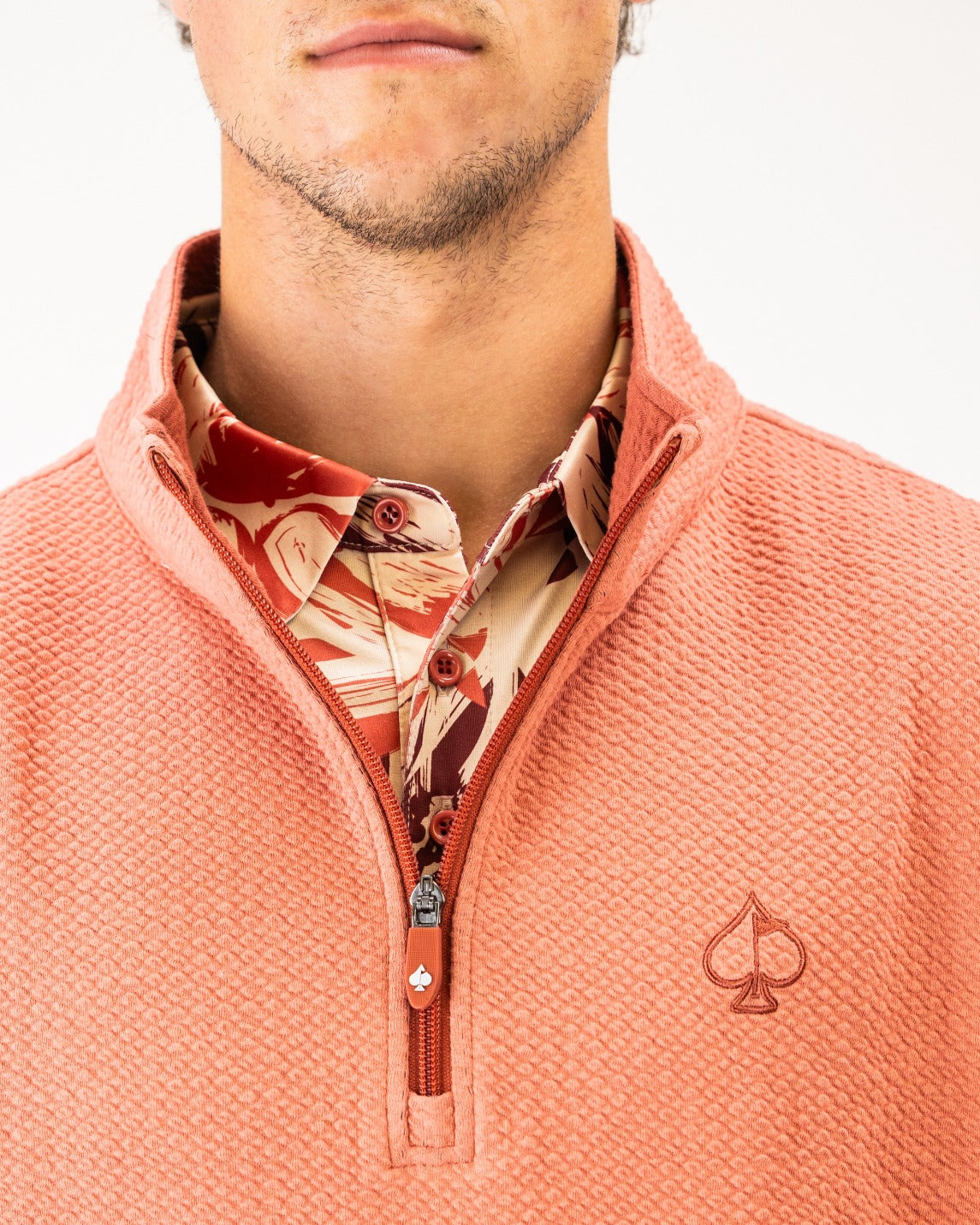 Terracotta waffle knit pullover with a half-zip collar, featuring a logo on the chest and a patterned shirt underneath.