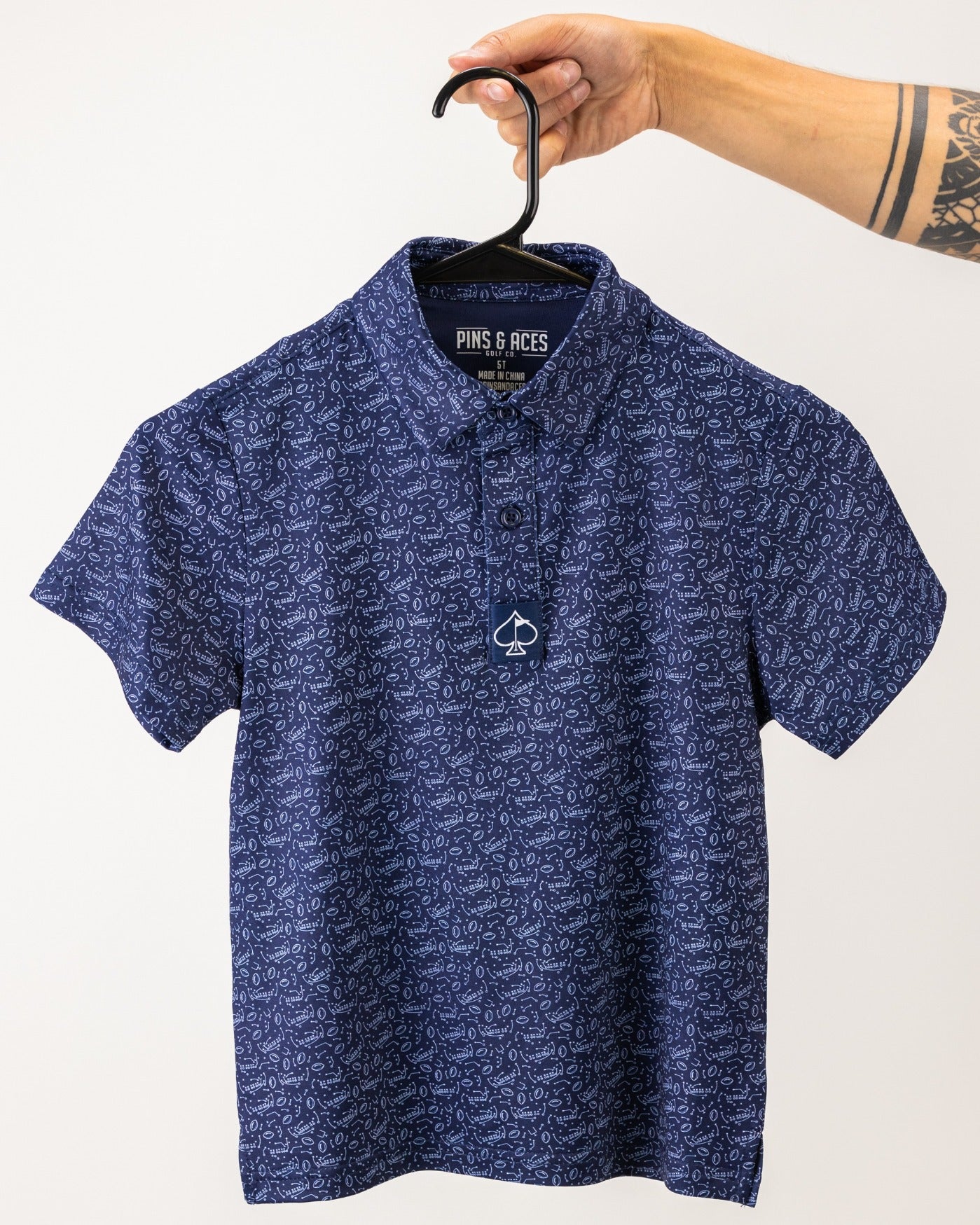 Navy blue youth golf polo shirt with a unique pattern, featuring a collar and a button placket, held by a hand.