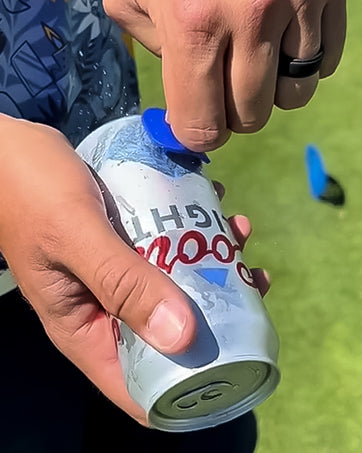 A golfer using The Shottee Golf Tee to open a beverage can on the course, showcasing its unique design and functionality.