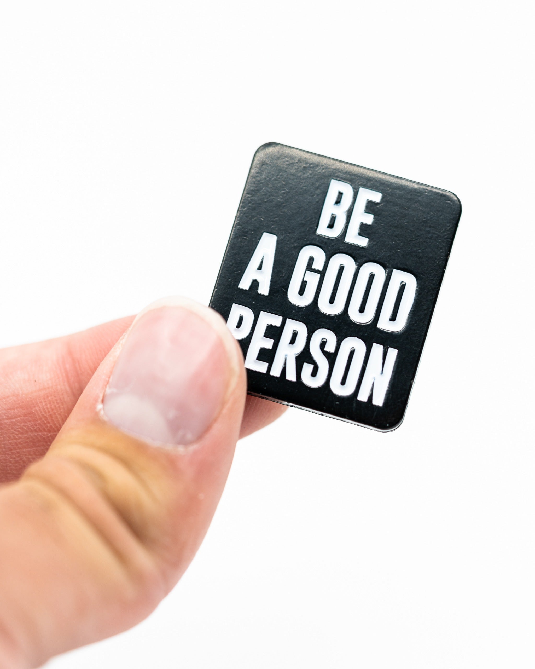 Black ball marker with the text "Be A Good Person" in bold white letters, held between fingers. Ideal for golfers.