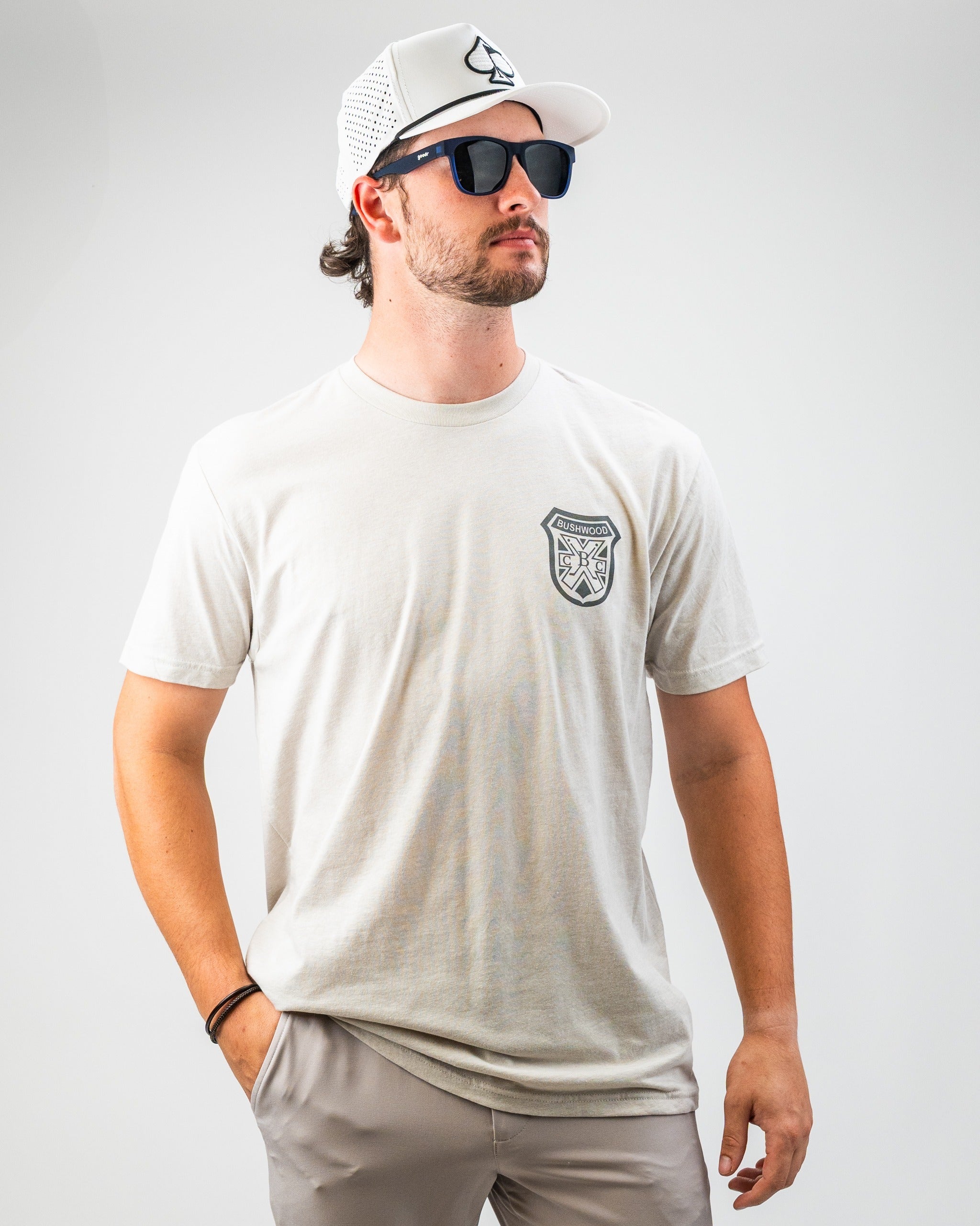 Men's Bushwood Crest 3.0 tee shirt in light color, featuring a logo patch on the chest, paired with sunglasses and a cap.