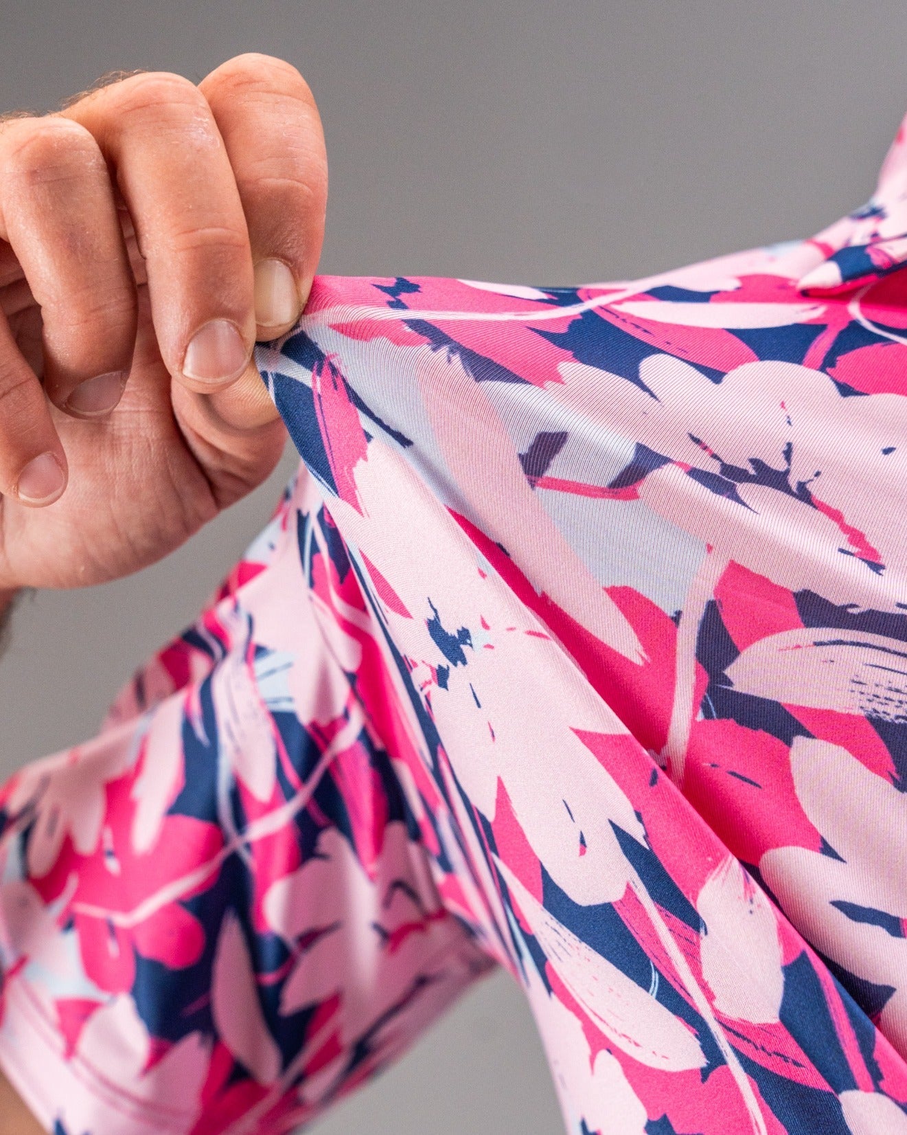 Close-up of pink, navy, and white floral-patterned golf apparel fabric being pulled to show its colorful, bold design.