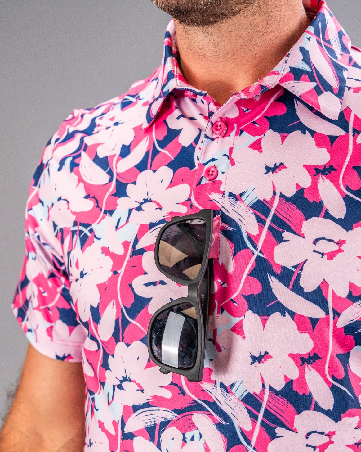 Bold pink, navy, and white floral golf shirt with sunglasses hanging from the collar, perfect for standing out on the course.