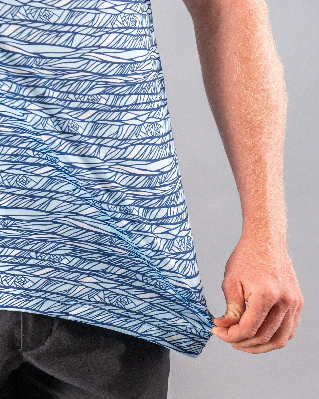 Close-up of a golfer's arm and shirt featuring bold, abstract blue and white line patterns, emphasizing unique golf apparel.
