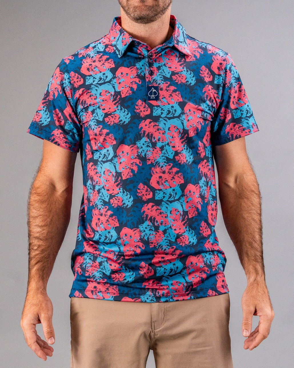 Colorful men's golf shirt with pink and blue tropical leaf pattern, collared, short sleeves, from a bold golf apparel brand.