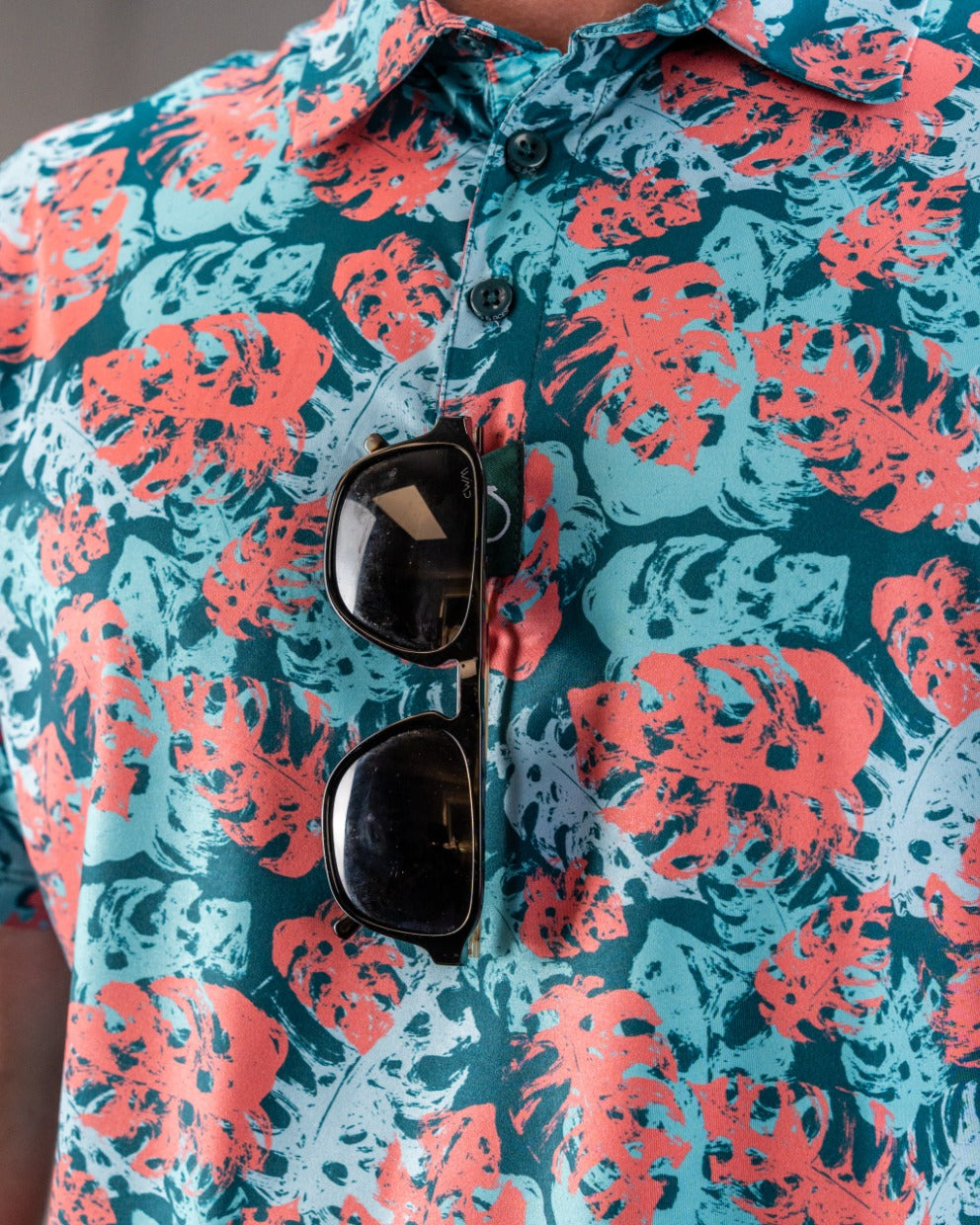 Bright blue and coral floral patterned golf shirt with sunglasses clipped to the front, perfect for bold golfers.