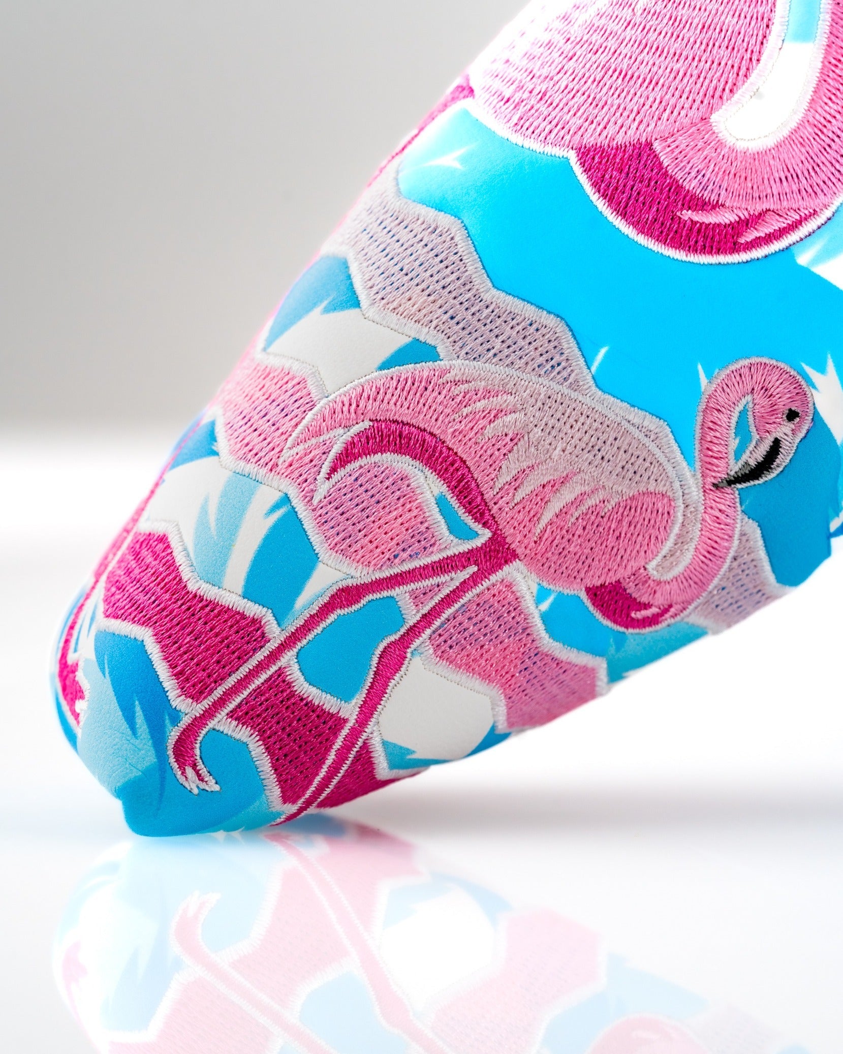 Colorful flamingo design on a blade putter cover, featuring vibrant pink and blue embroidery for a bold golf accessory.