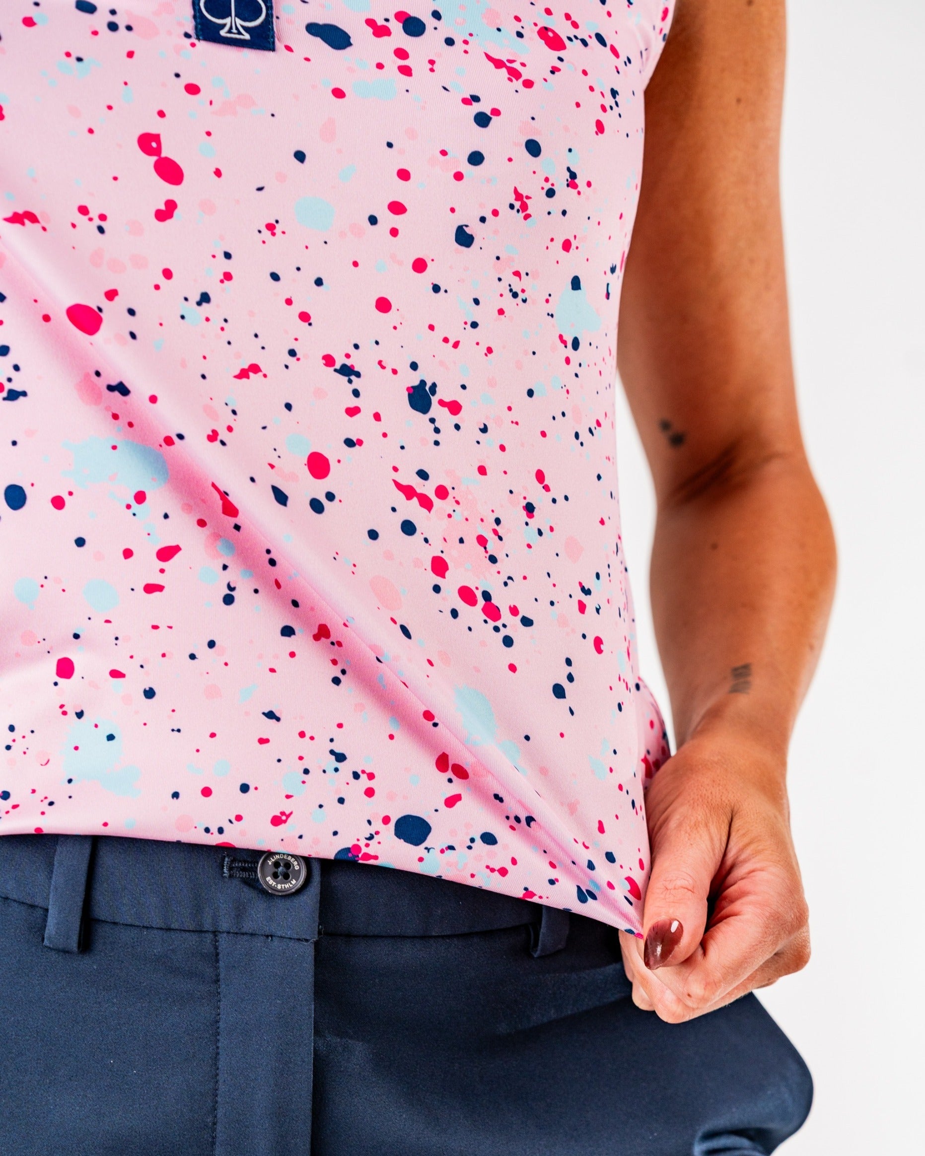 Women's pink splatter golf top featuring a vibrant design with colorful splashes, paired with navy golf pants.