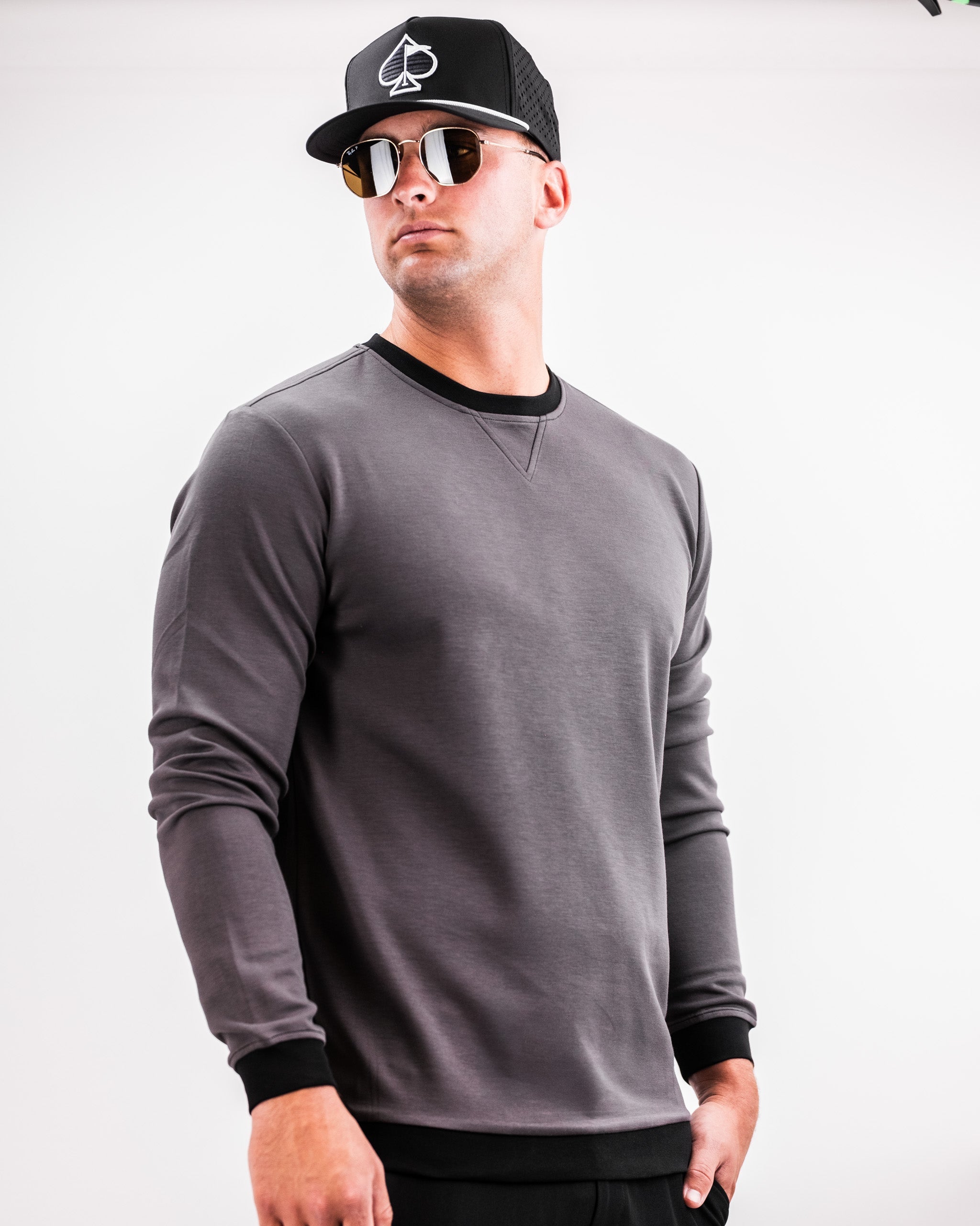 Male model wearing a slate grey Player Preferred™ Crewneck sweatshirt with black accents, black cap, and sunglasses, standing against a white background.