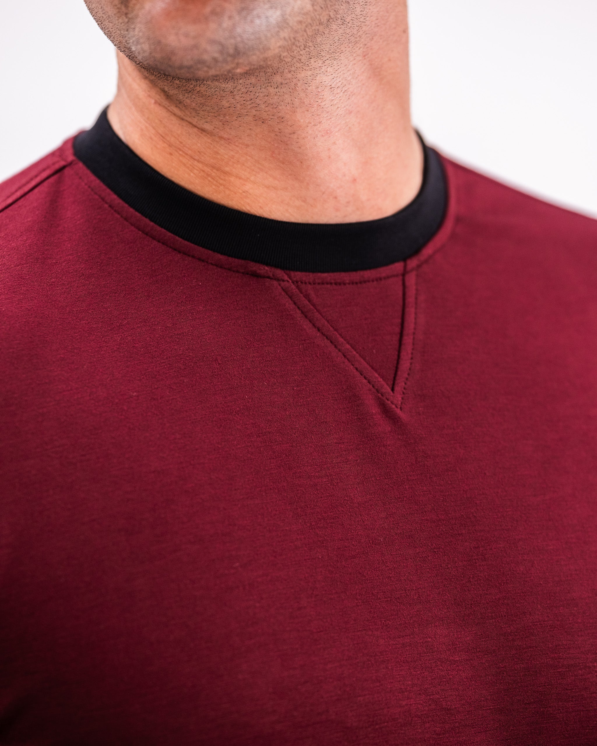 Close-up of a man wearing a maroon Player Preferred™ Crewneck with a black neckline detail, highlighting the fabric and stitching.