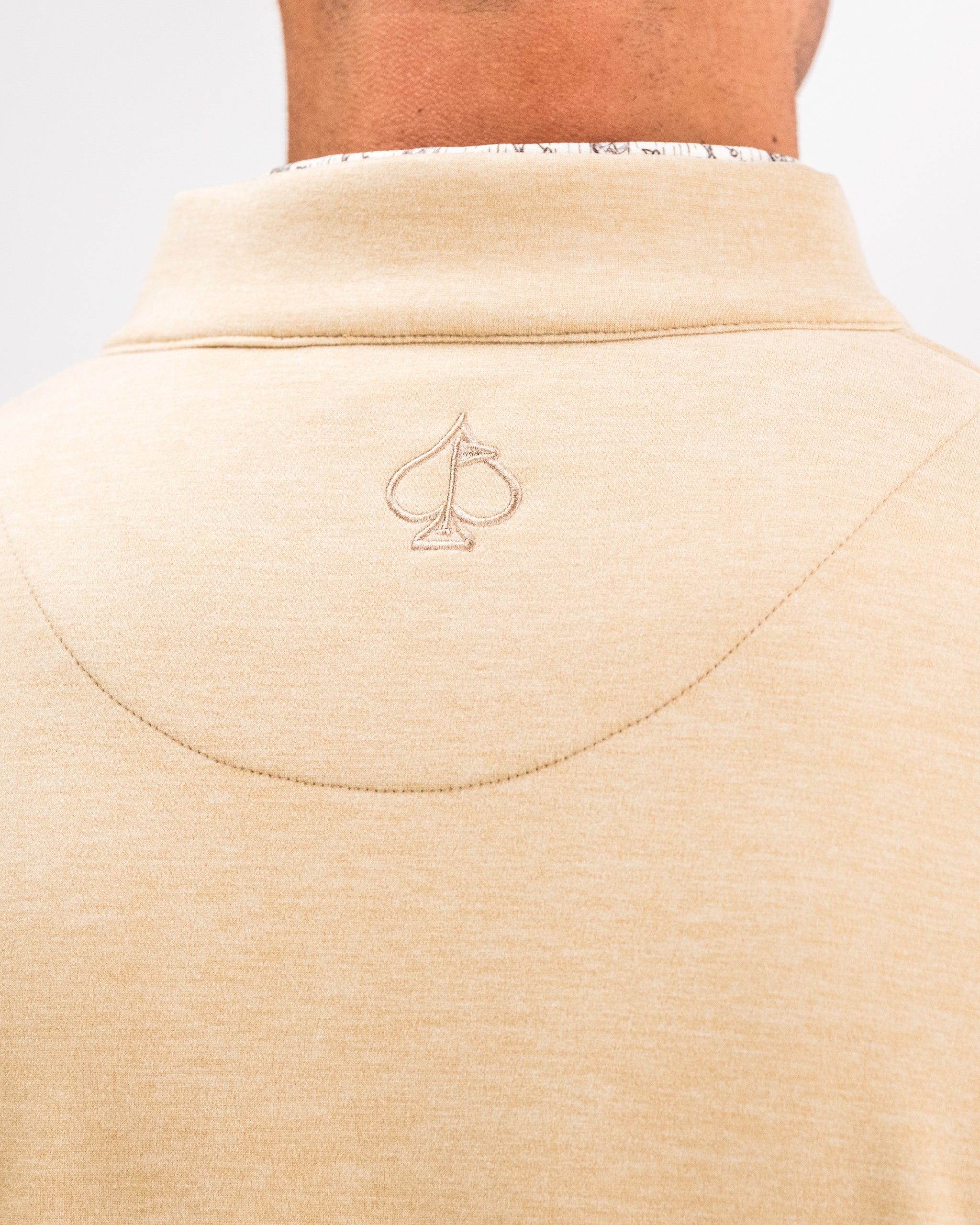 Close-up of the back of a beige Player Preferred™ Pullover with a small embroidered spade logo near the collar.