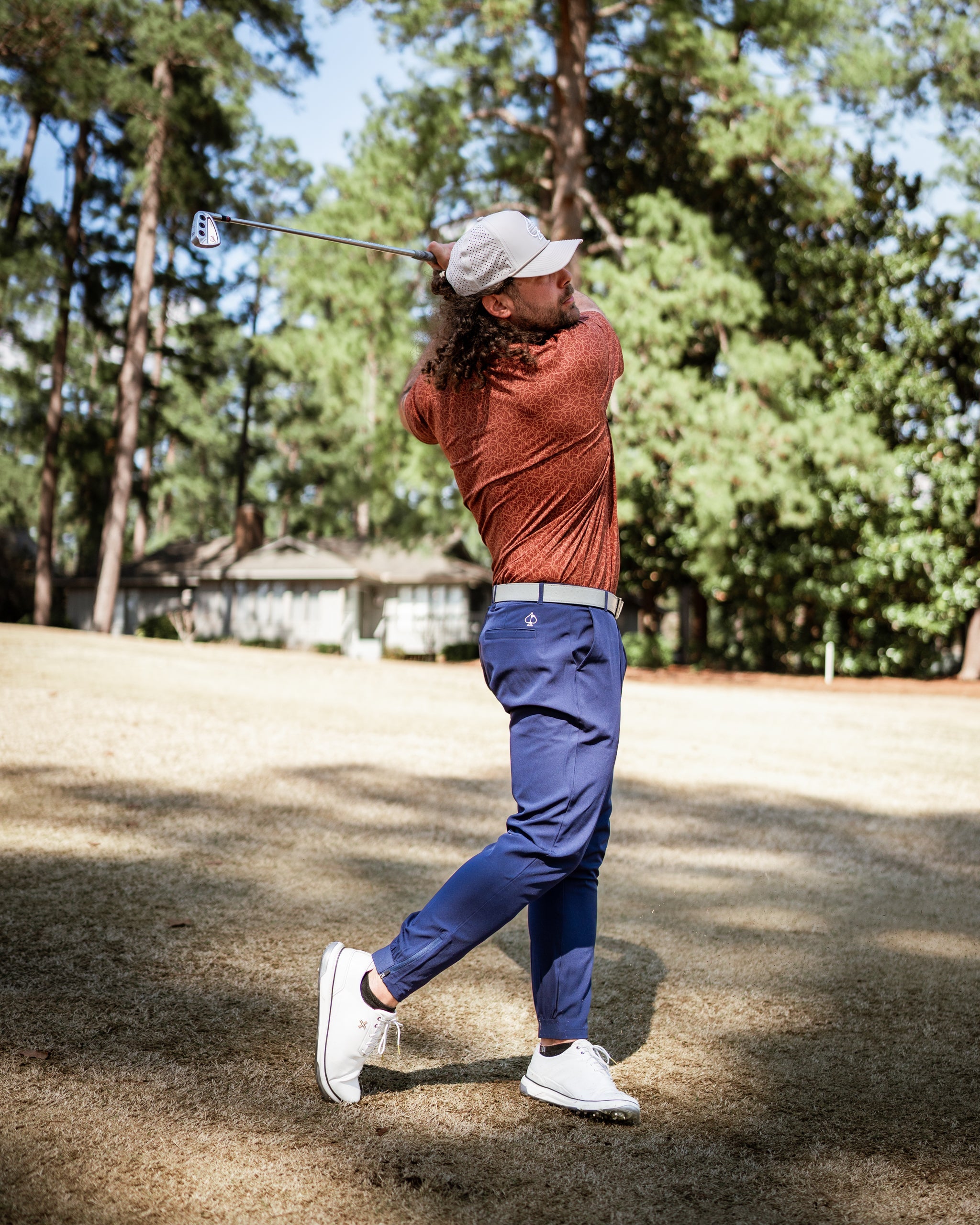 A golfer swings a club on the course, wearing a stylish orange shirt and navy pants, showcasing bold golf apparel.