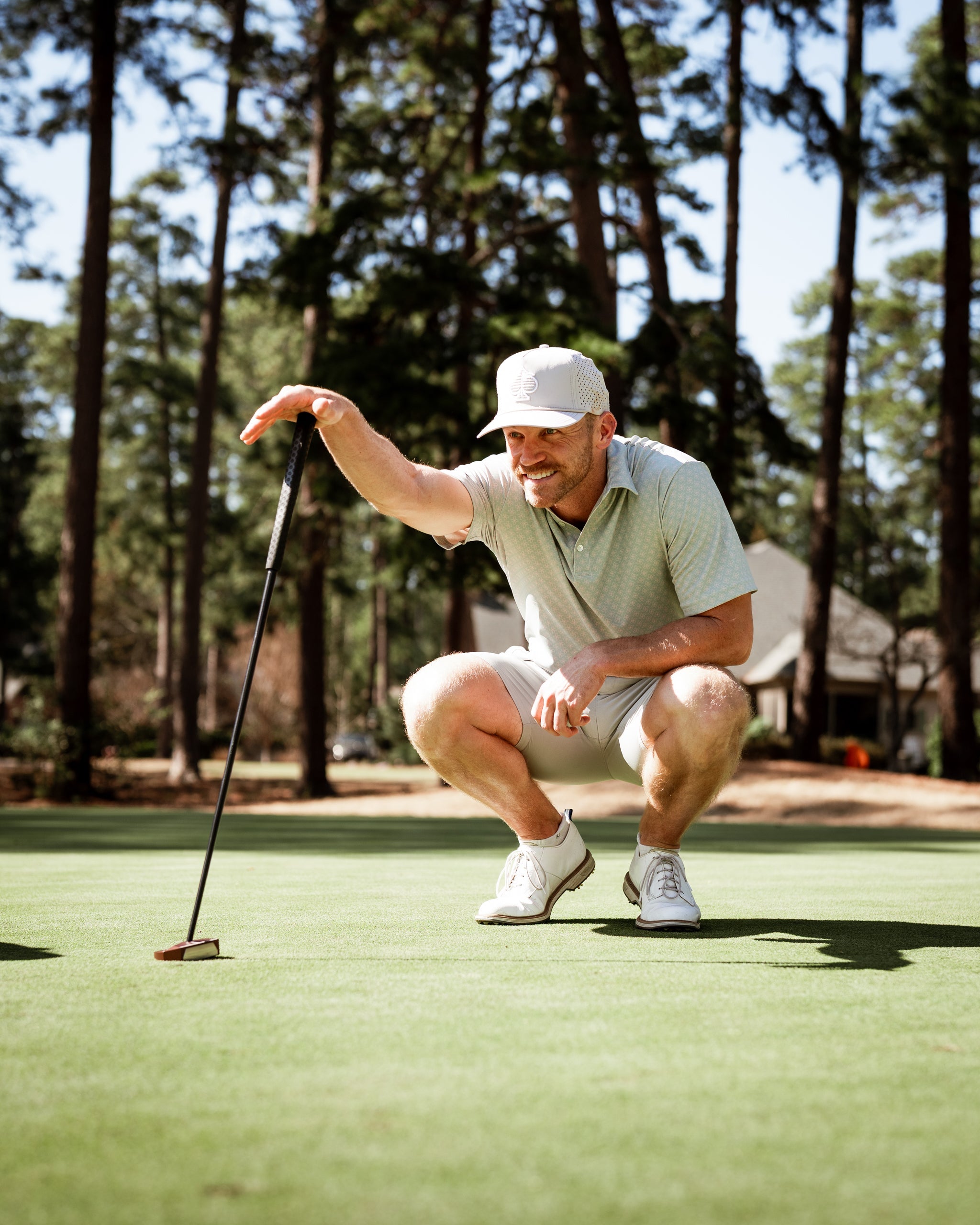 A golfer in a light green polo and cap crouches on the putting green, focusing intently on his putt.