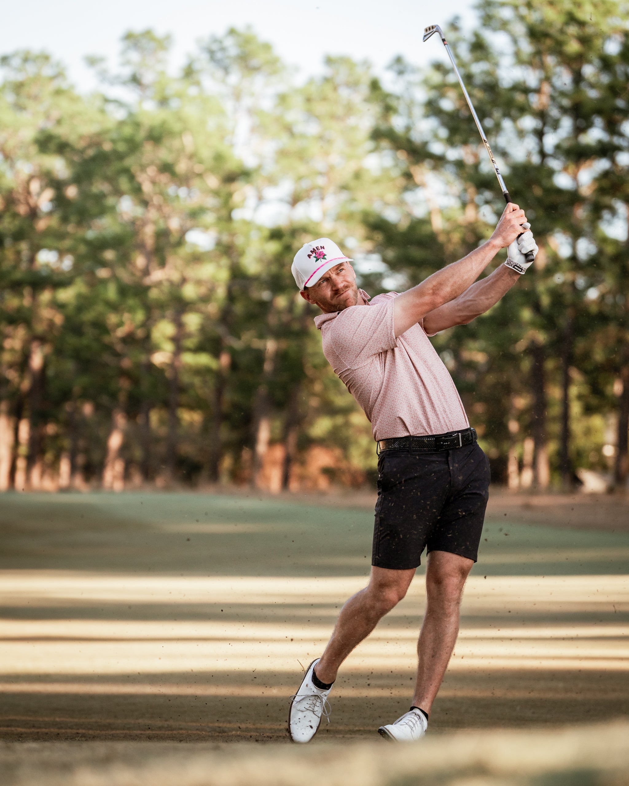 Golfer in a stylish polo and shorts swings a club on a sunny course, showcasing bold golf apparel from Pins and Aces.