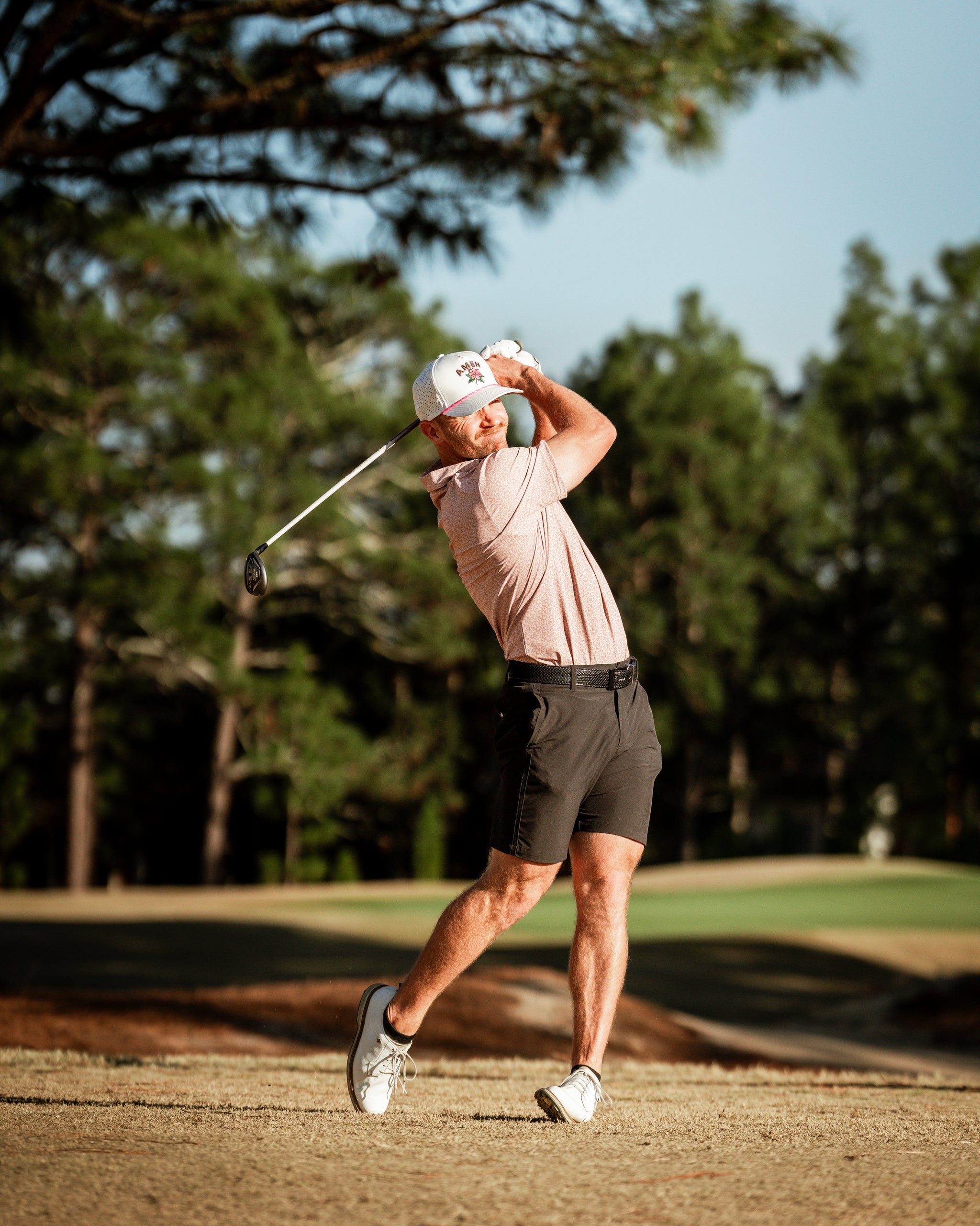 A golfer swings a club on the course, wearing a stylish pink polo and shorts, showcasing bold golf apparel.