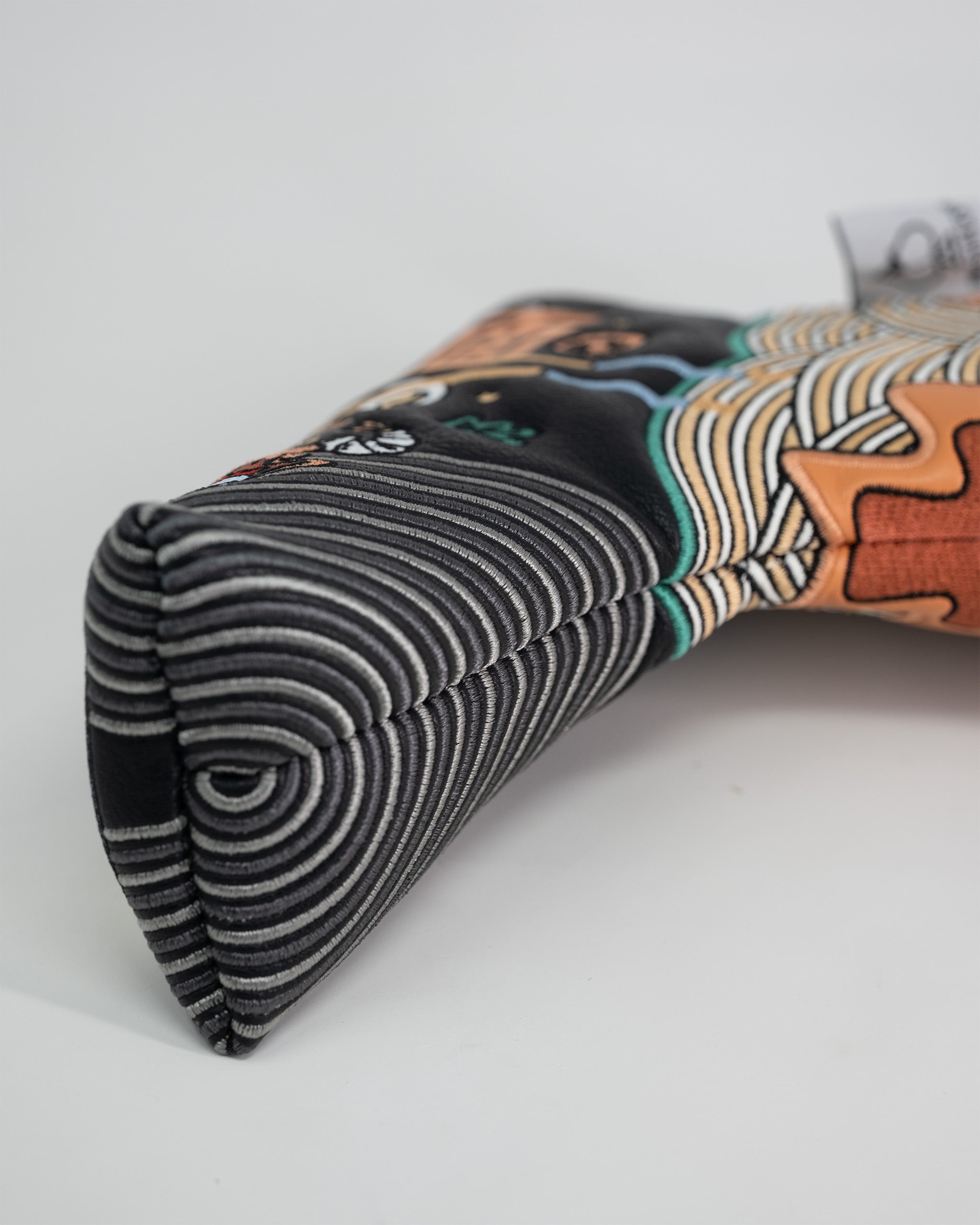 Close-up of a ramen-themed blade putter cover with black and white striped fabric, detailed embroidery, and colorful design elements.