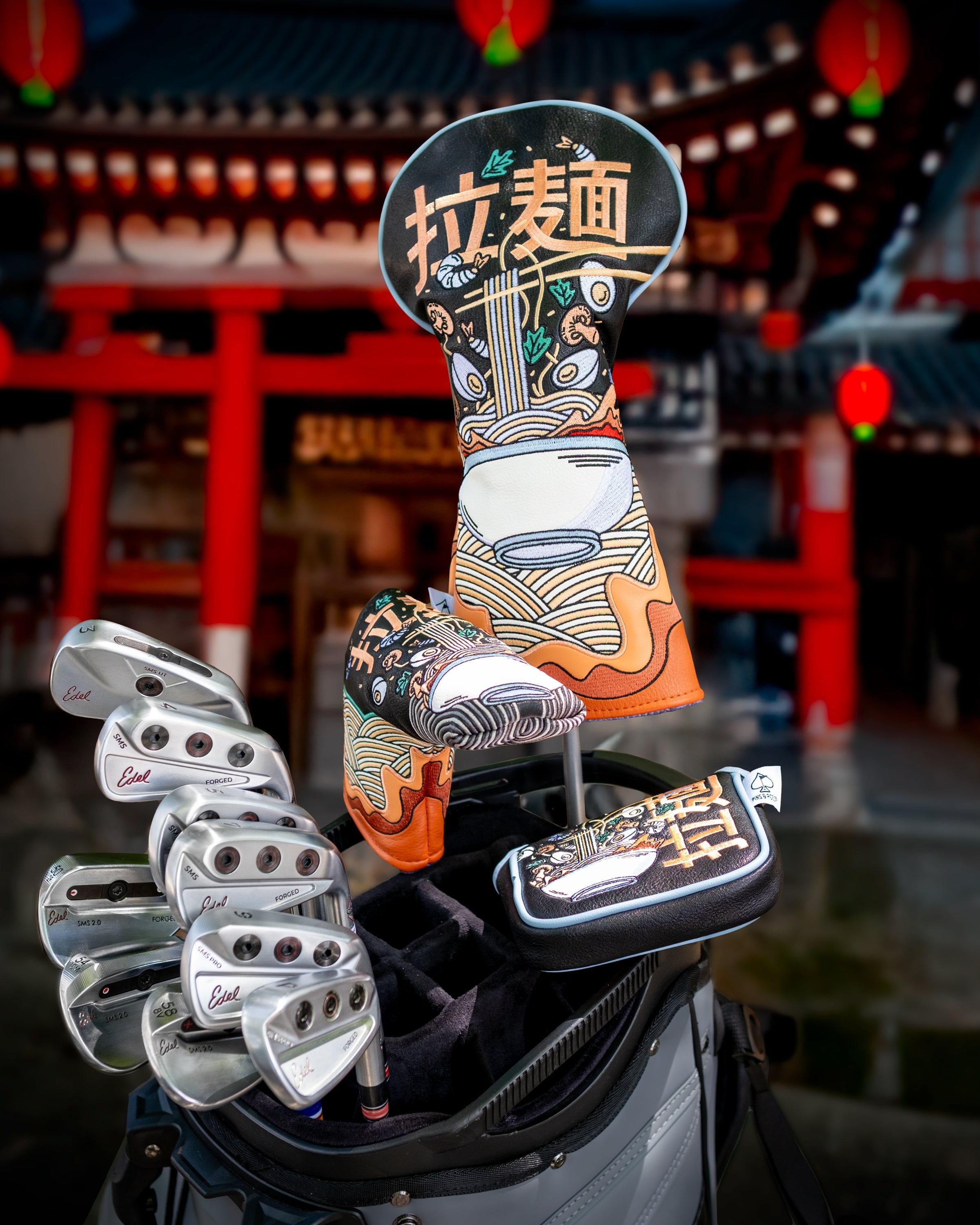 Golf driver cover featuring a colorful ramen bowl design, placed on a golf bag with clubs against a traditional Asian temple background.