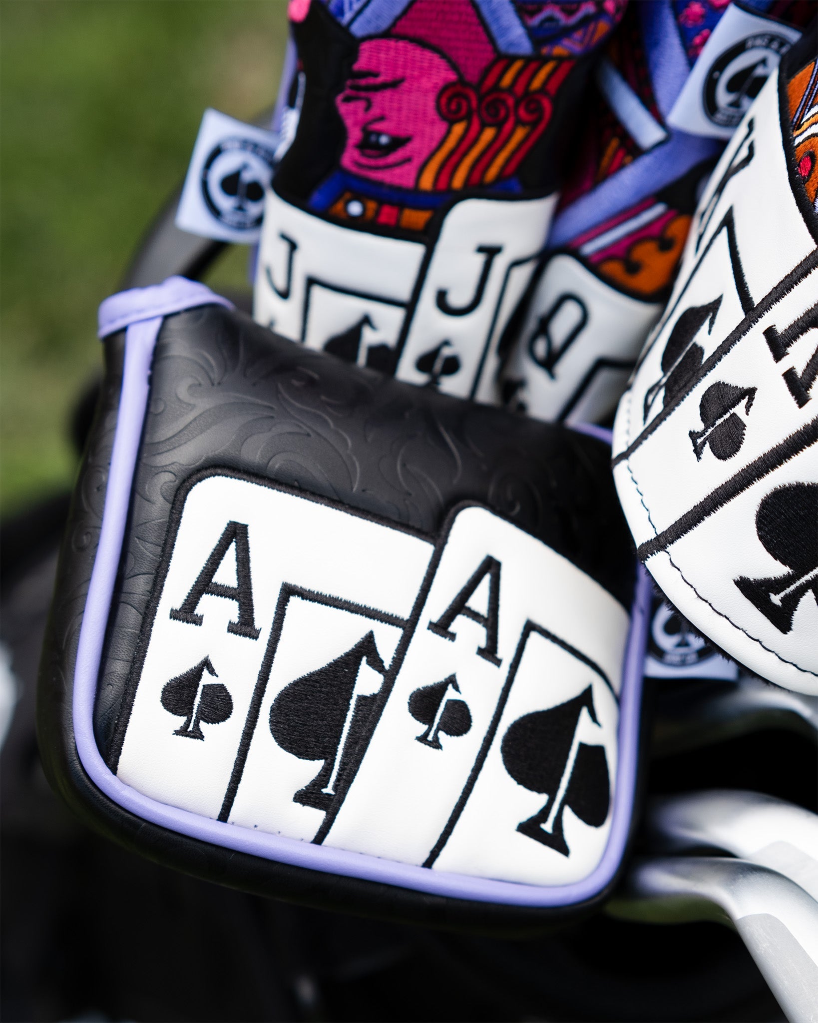 Black and white Ace of Spades mallet putter cover with embossed designs, prominently displayed among other colorful golf club covers.