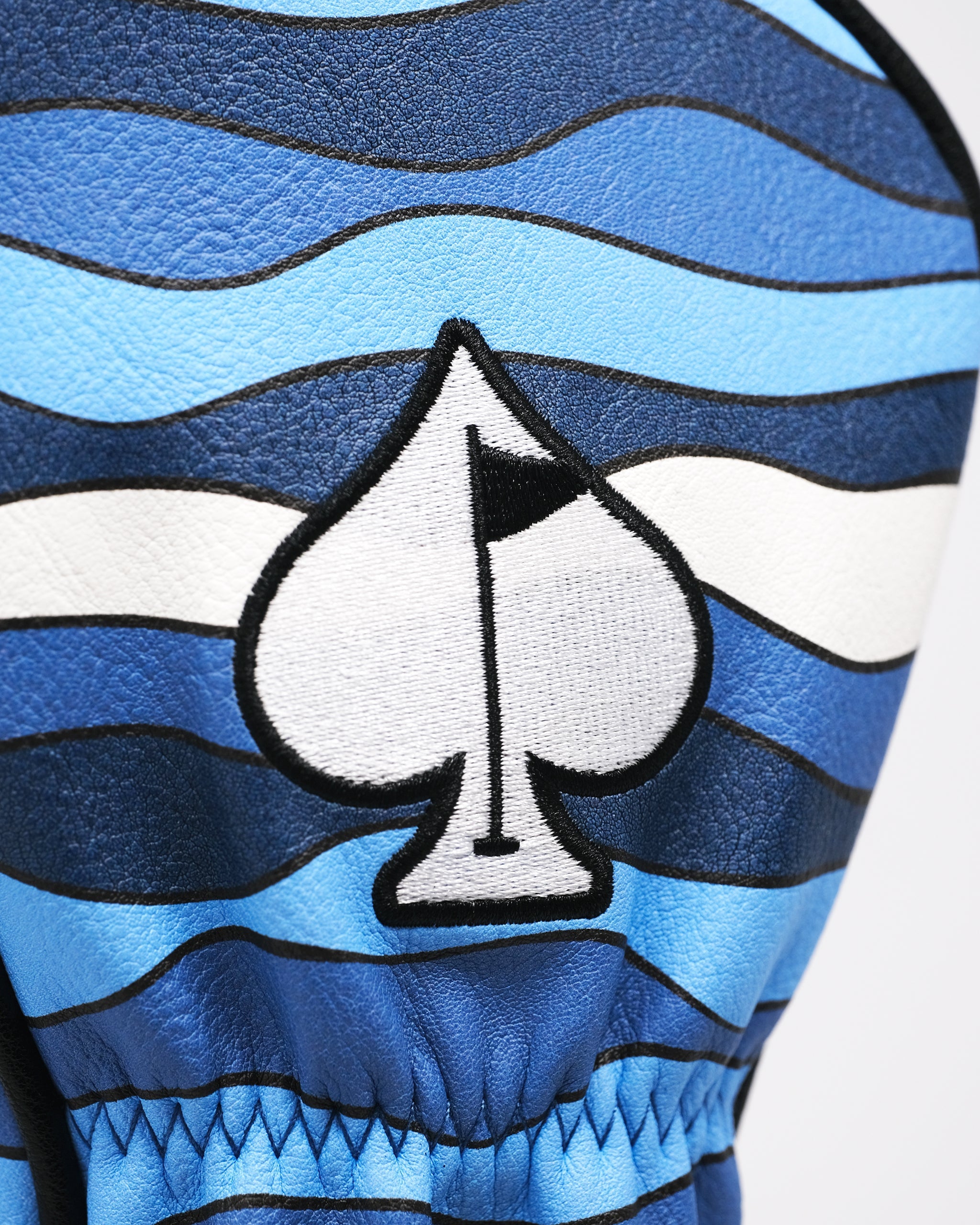 Close-up of a bold blue and white golf headcover with a spade logo, black outlines, and wavy striped pattern for standout ...