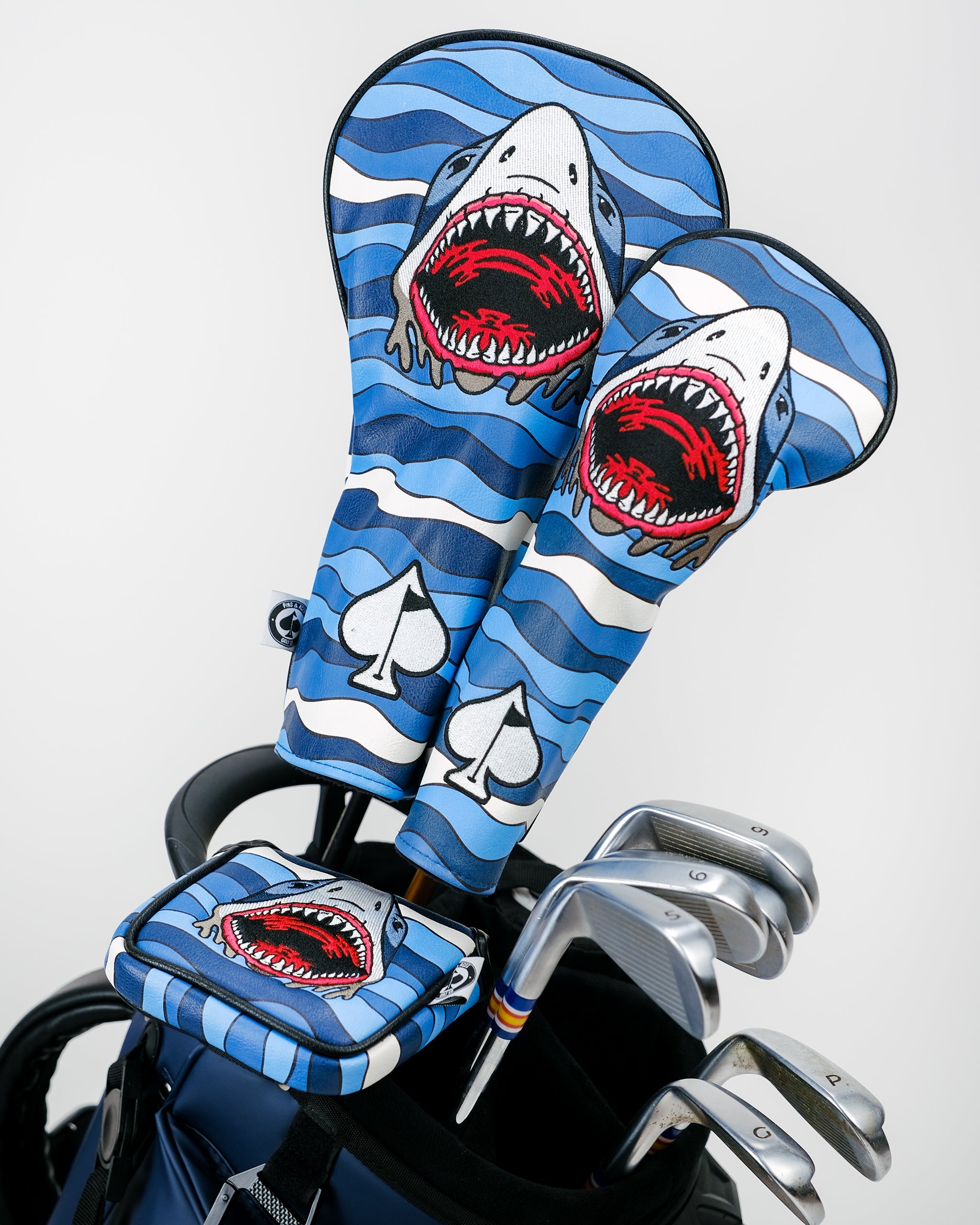Bold blue shark-themed golf headcovers with red mouths, white spade accents, and matching accessories for standout style.