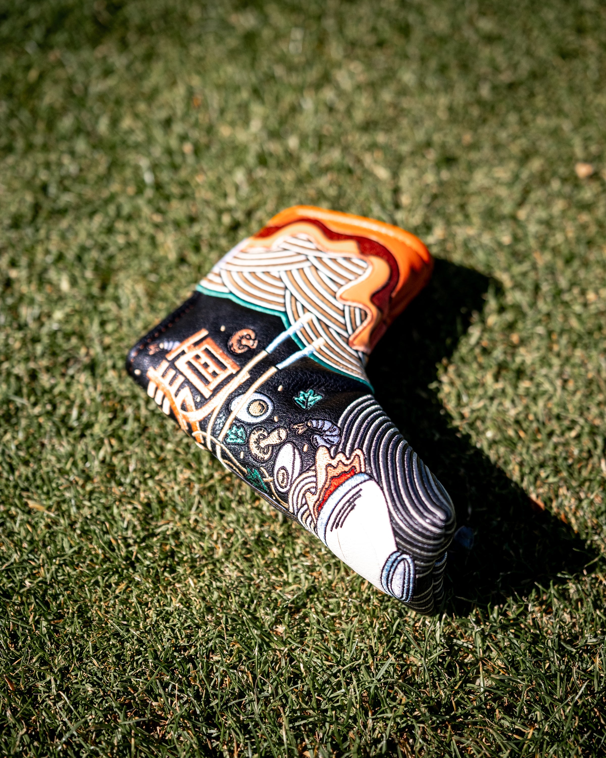 Colorful ramen bowl design Blade Putter Cover resting on grass, protecting golf club heads with vibrant, detailed artwork.