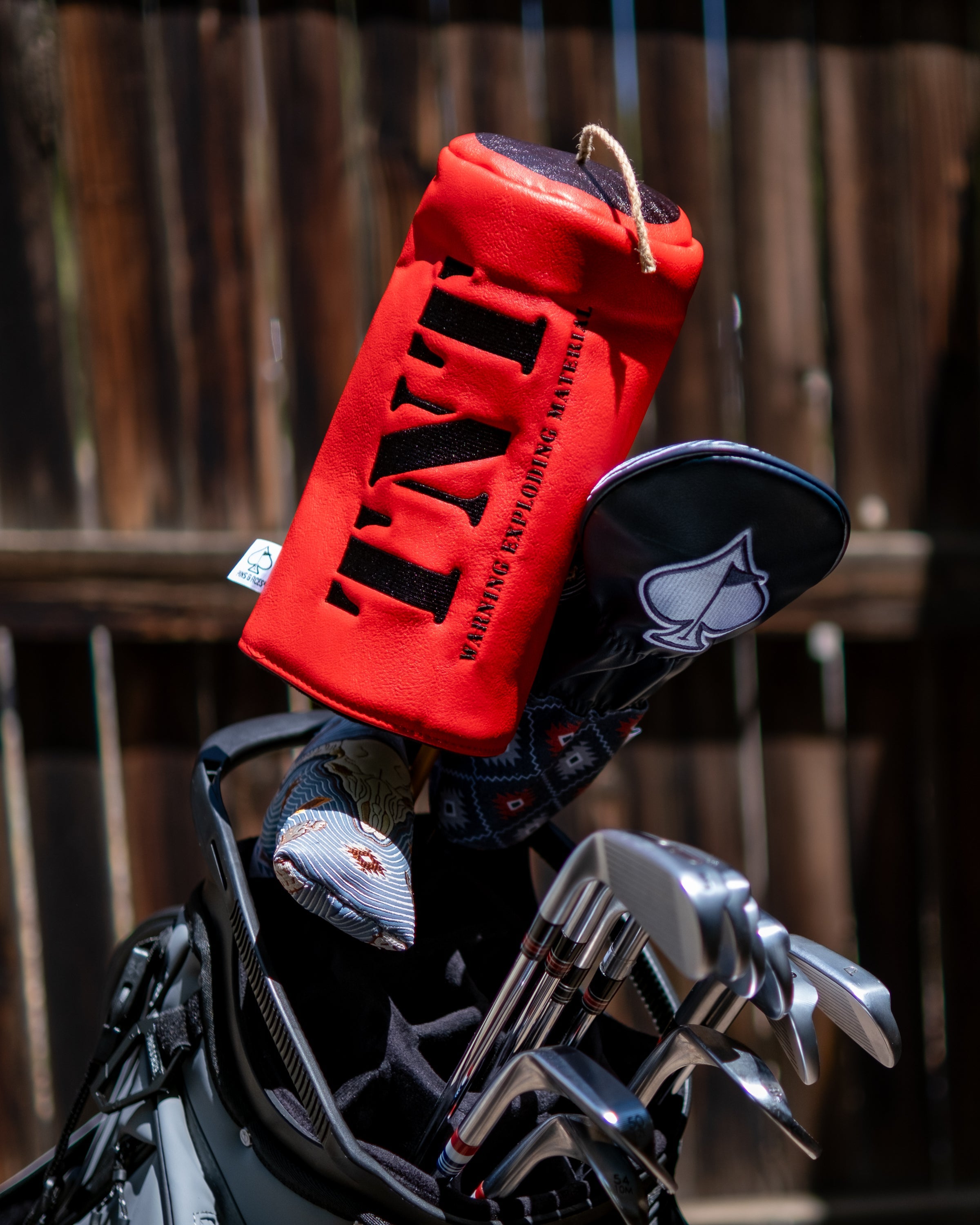 Red TNT driver golf club cover with black lettering, attached to a golf bag containing clubs and other accessories.