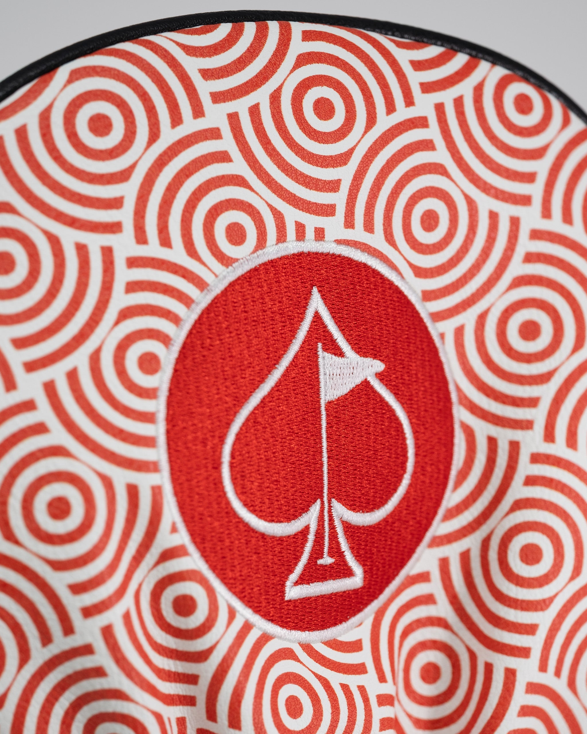 Close-up of a red and white spade logo embroidered on a patterned driver cover with concentric circle designs.