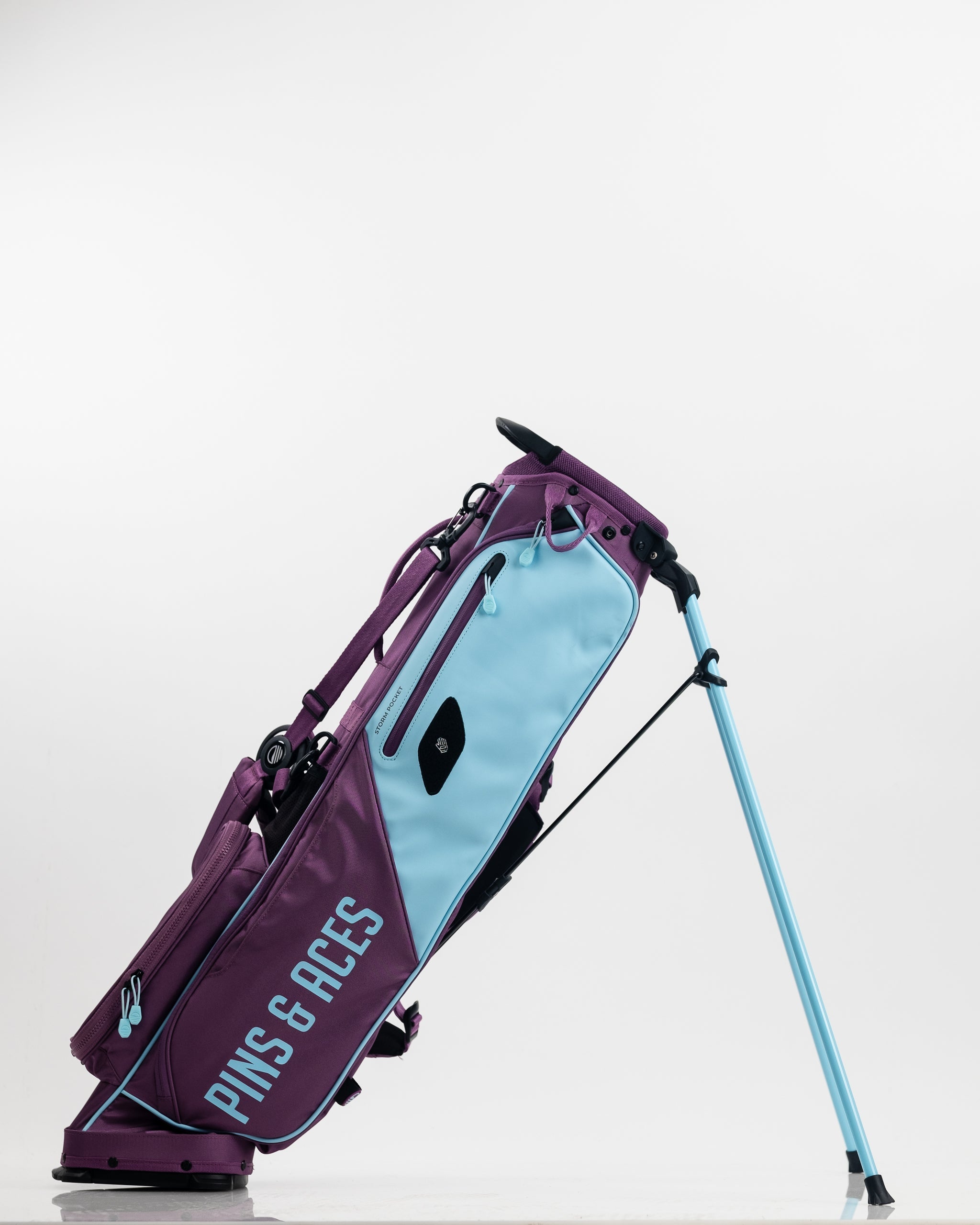 Colorful golf bag in purple and light blue with "PINS & ACES" branding, featuring bold design for standout golf style.