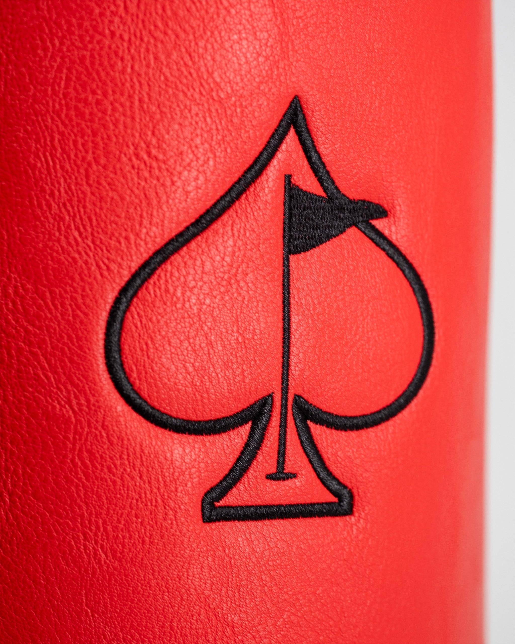 Close-up of a red golf driver cover featuring a black embroidered spade symbol with a small flag at the top.
