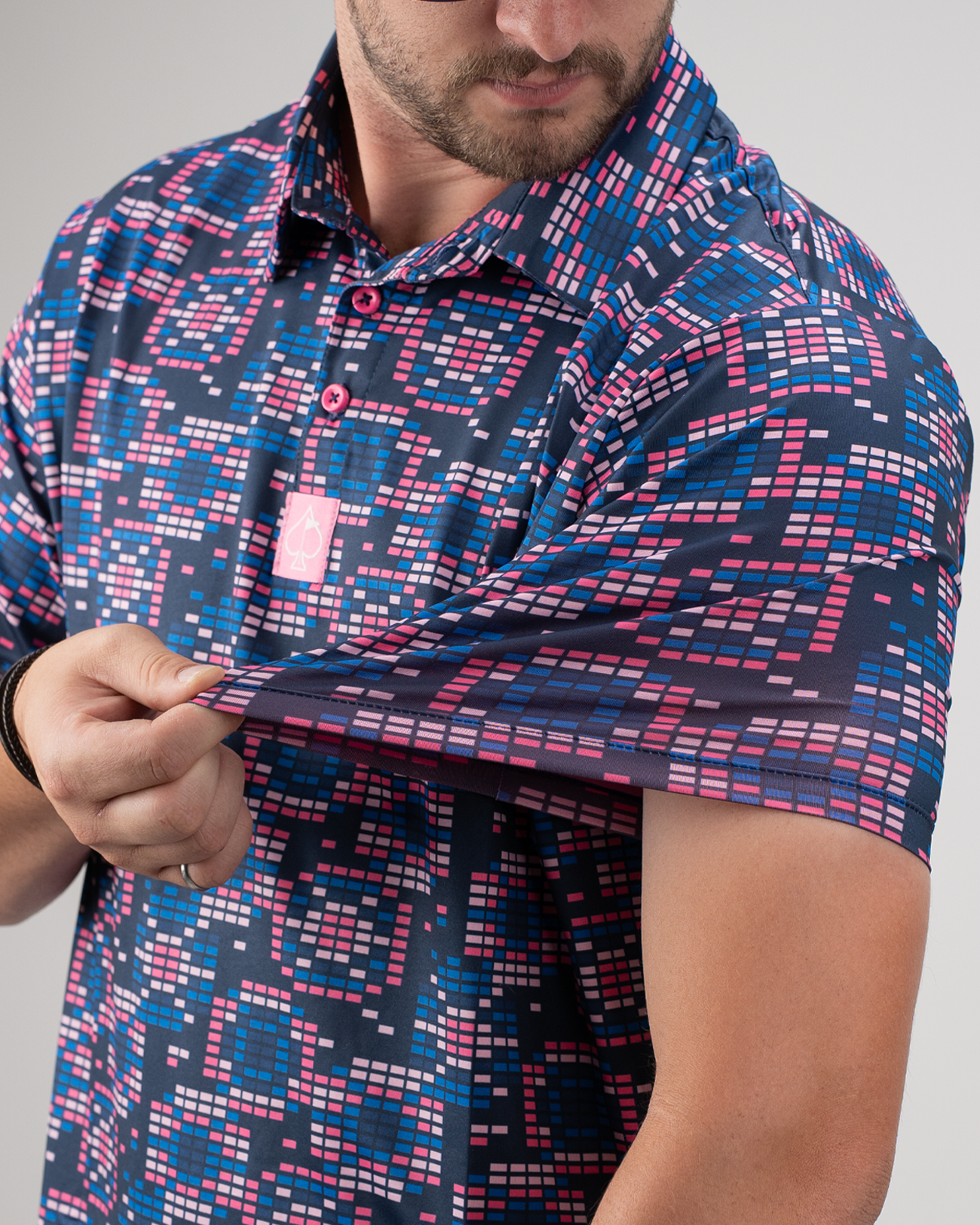 Model showcasing the Tetrafloral Dark golf polo shirt with a vibrant geometric pattern in navy, pink, and blue tones.