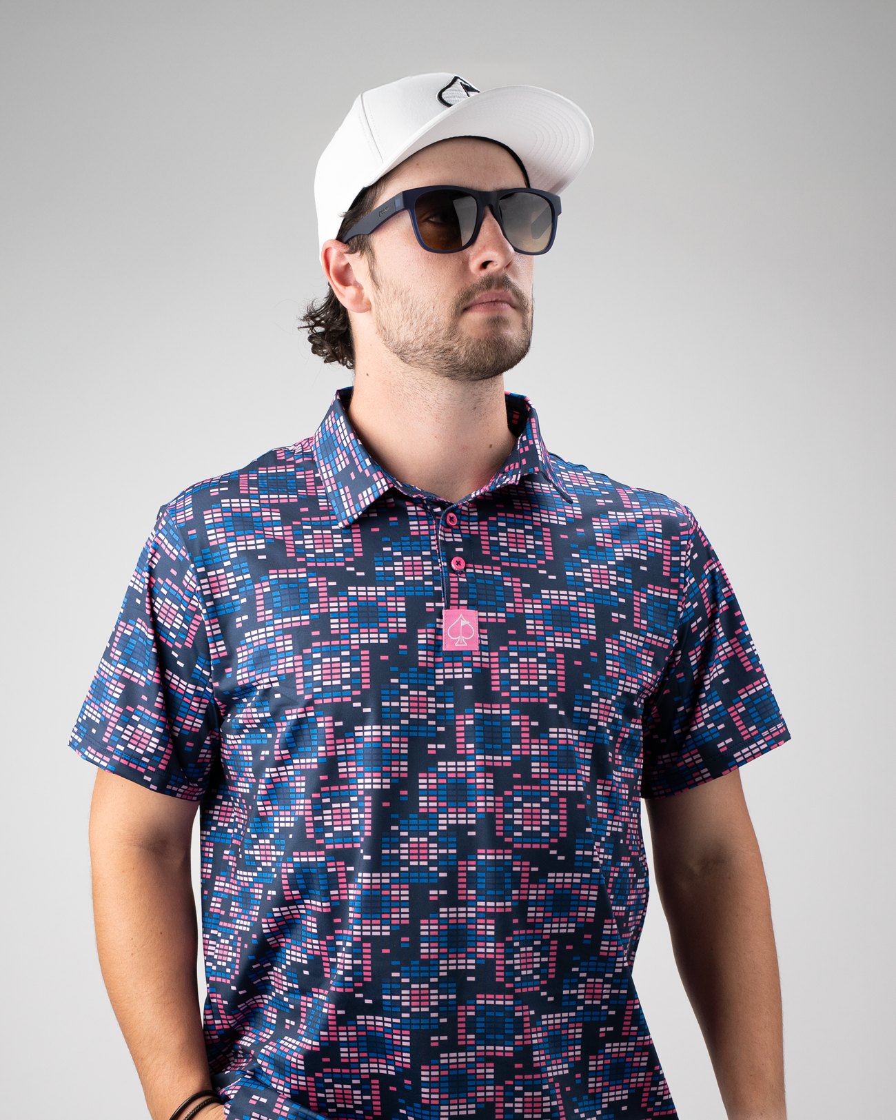 Man wearing a Tetrafloral Dark golf polo with a vibrant geometric pattern, paired with sunglasses and a white cap.