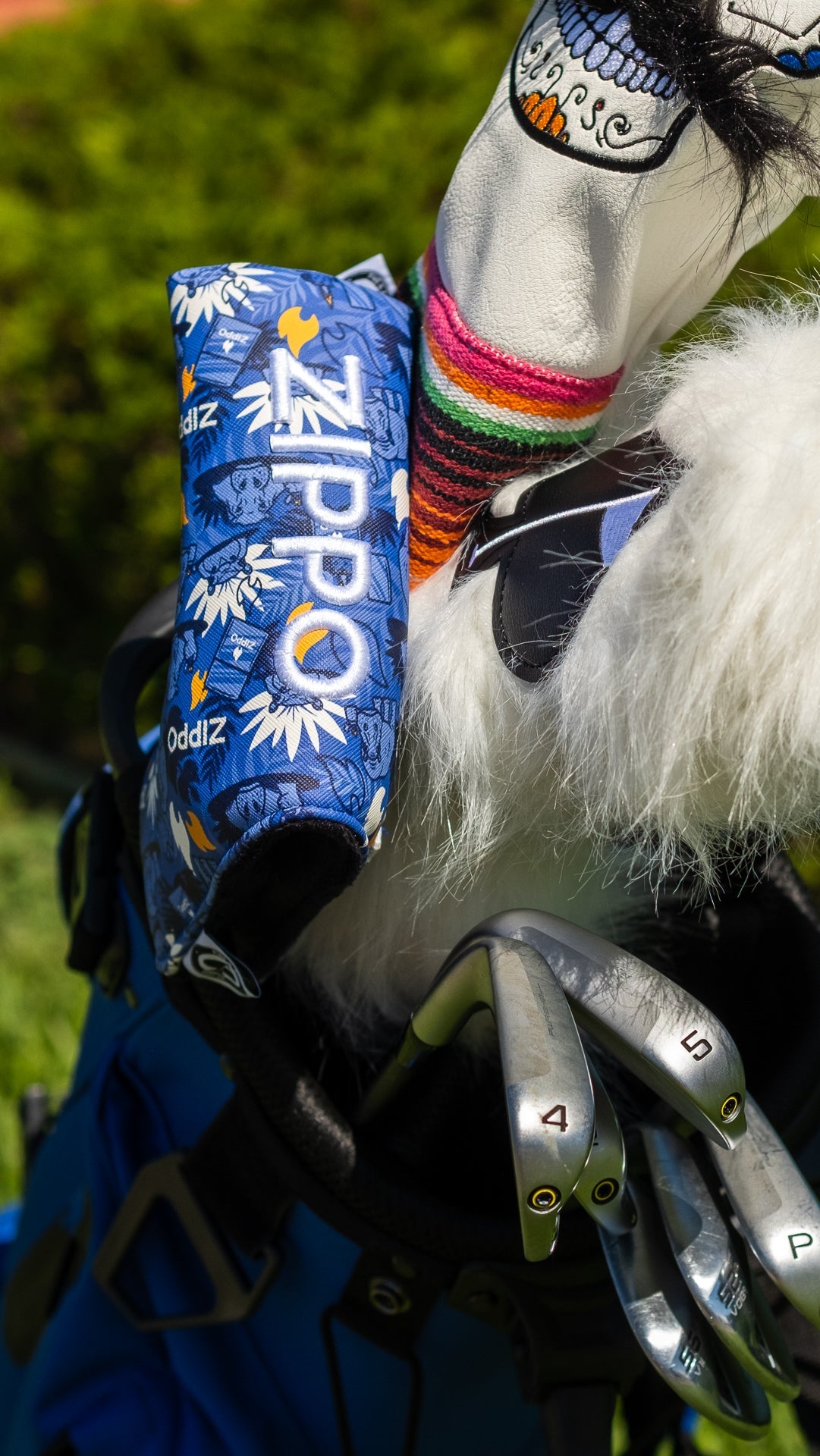 Blue Zippo Blade Putter Cover with graphic design, attached to a golf bag with clubs and colorful socks in the background.