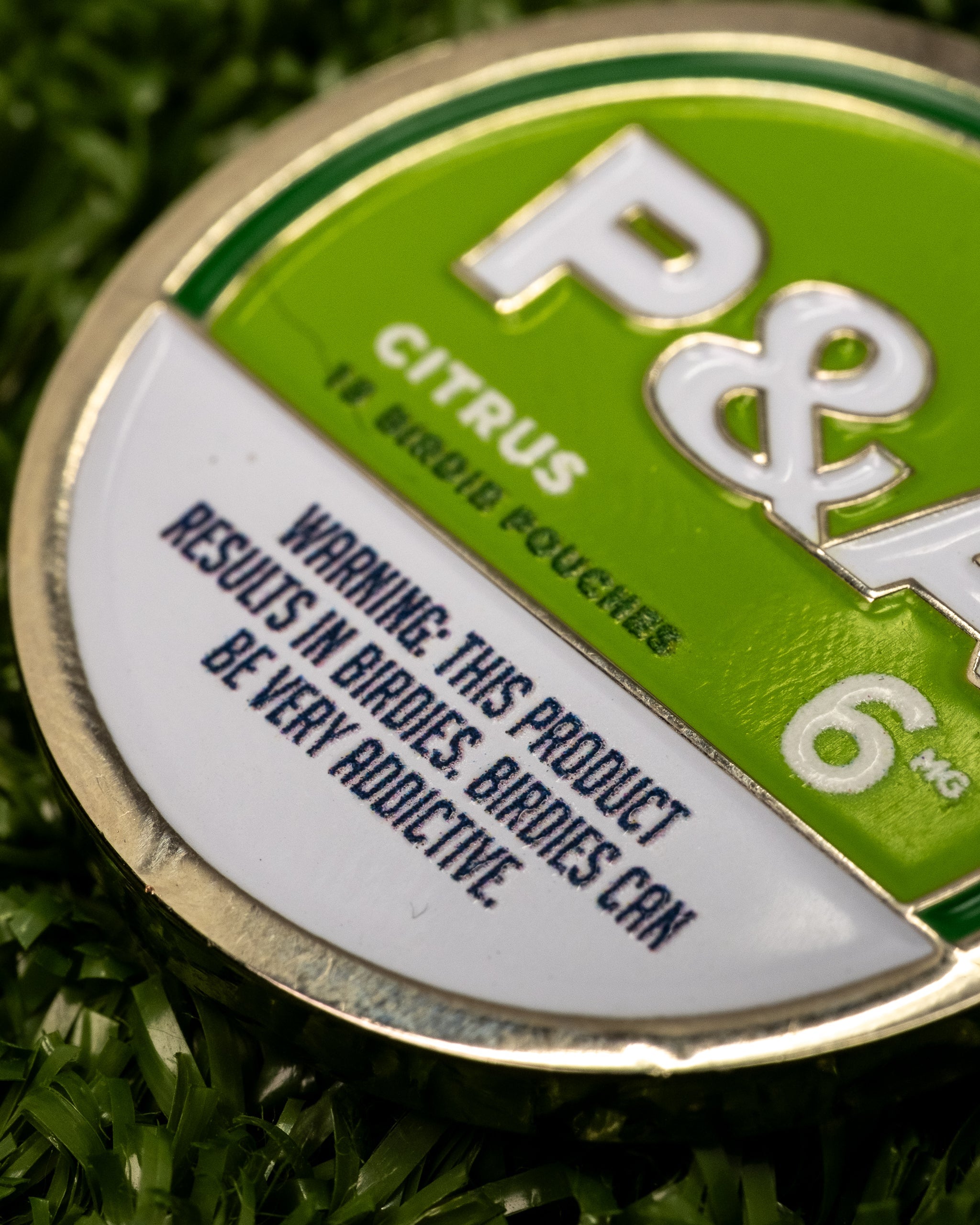 Close-up of a 6 Milly Citrus Ball Marker, featuring a warning about its addictive nature for birdie enthusiasts.