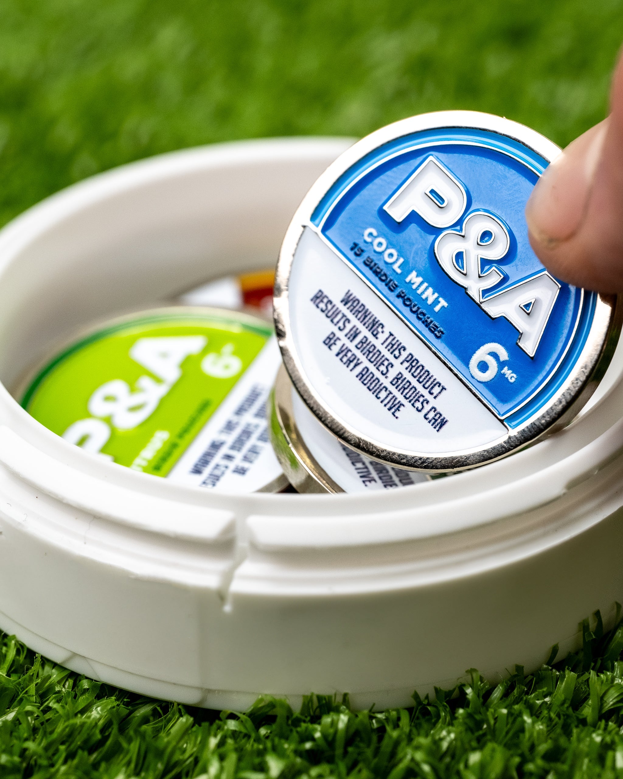 "6 Milly Cool Mint ball marker in a round container, showcasing vibrant packaging on green grass.