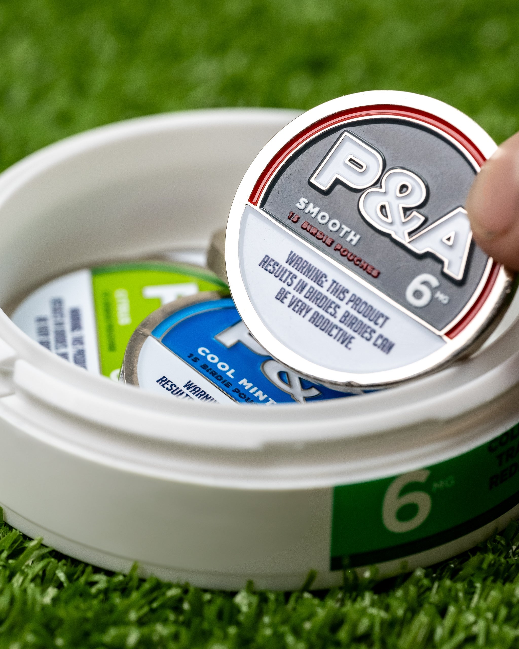 Close-up of a hand holding a 6 Milly Smooth Ball Marker, with other markers visible in a round container.