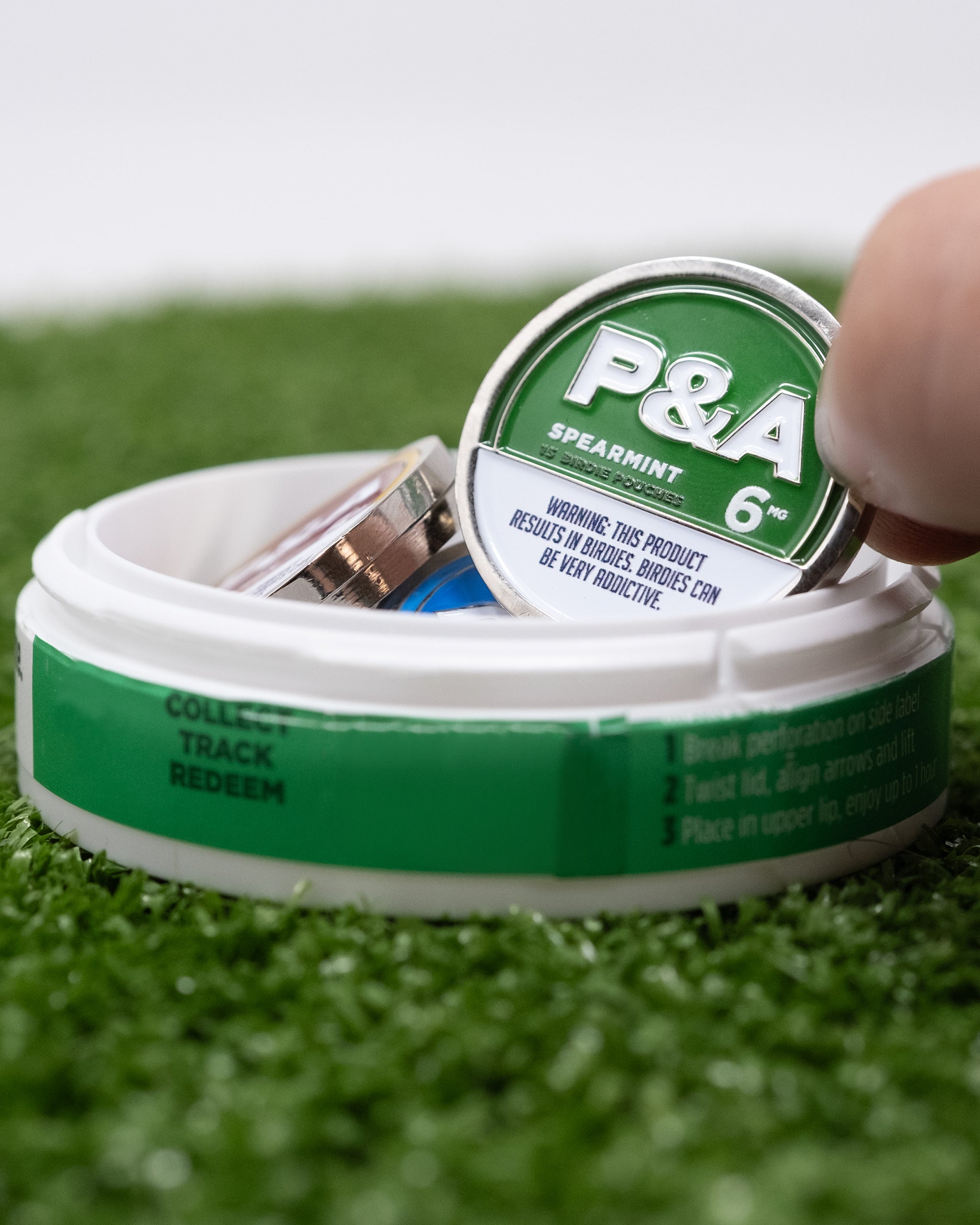 "6 Milly Spearmint ball marker being removed from a container on green turf.
