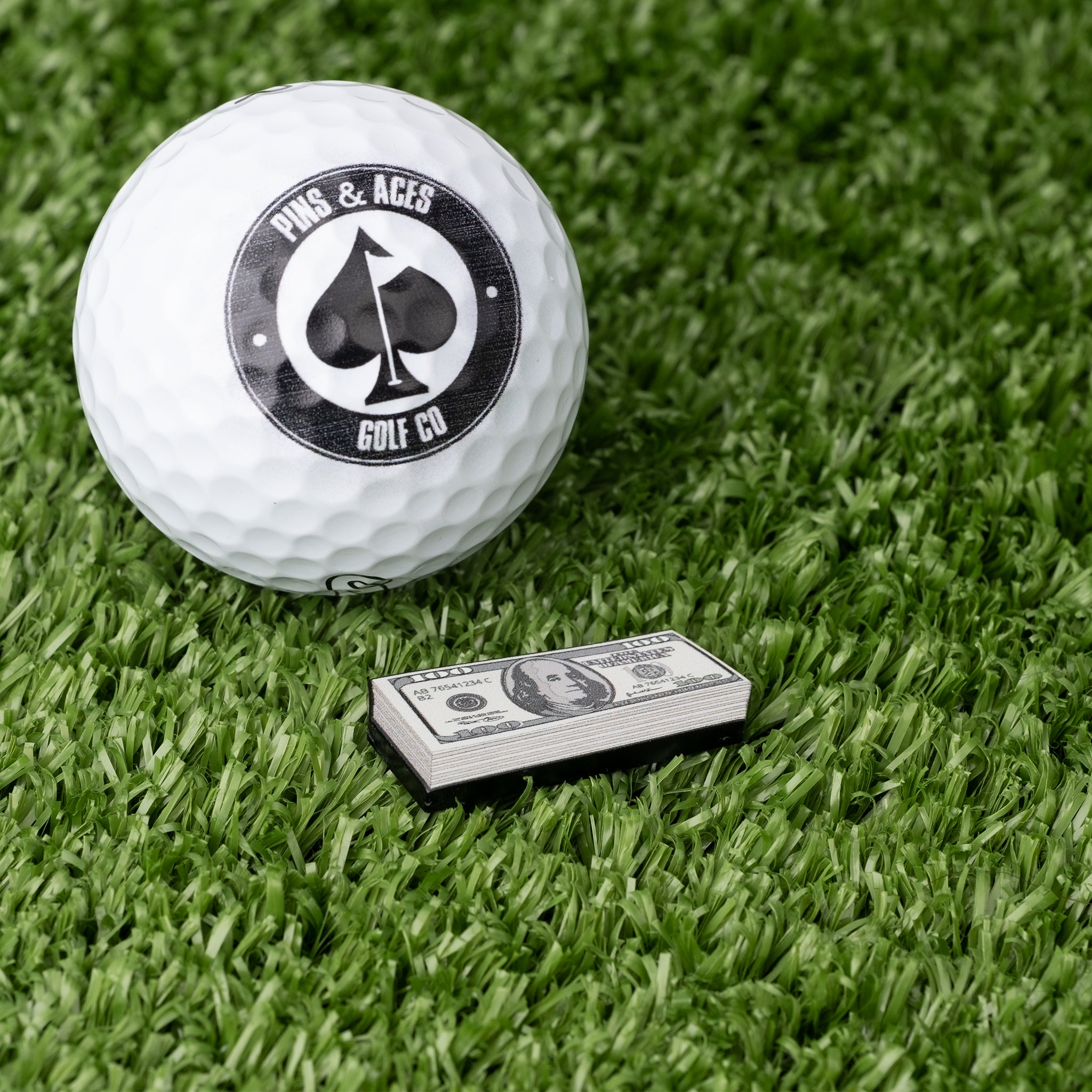 Cash Stack Ball Marker featuring a vibrant design with stacked bills, placed next to a golf ball on a putting green.