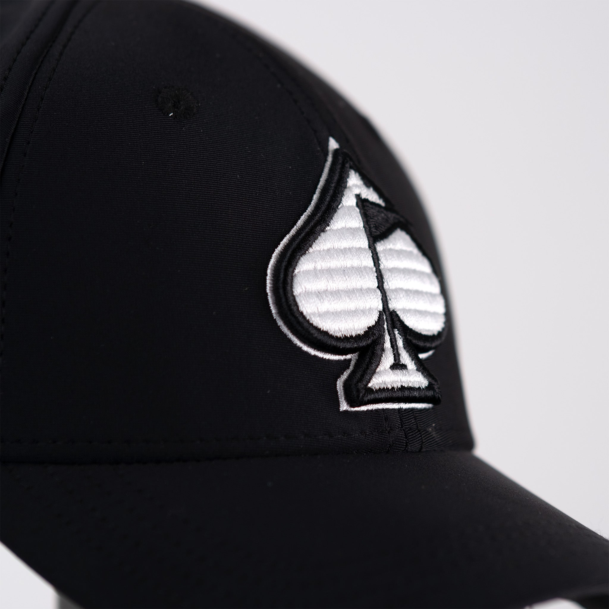 Fitted black performance hat featuring a white embroidered spade logo, designed for stylish golfers on the course.
