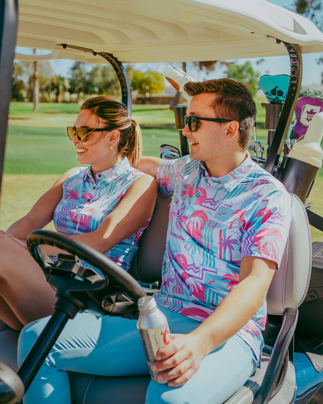 Couple in vibrant Beach Party golf shirts enjoying a sunny day on the golf course, seated in a golf cart.