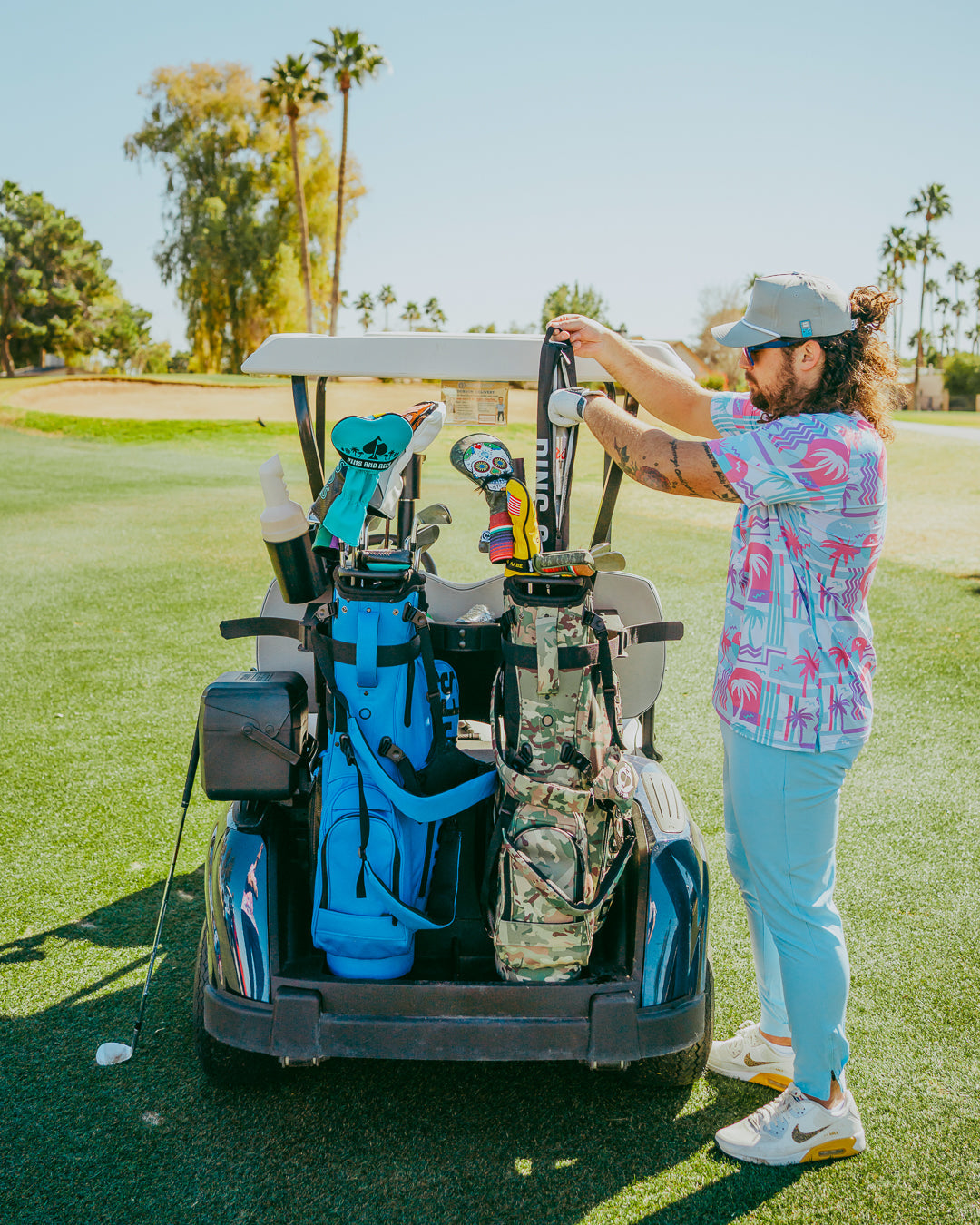 A golfer adjusts equipment on a golf cart, showcasing vibrant beach-themed apparel and colorful golf accessories.