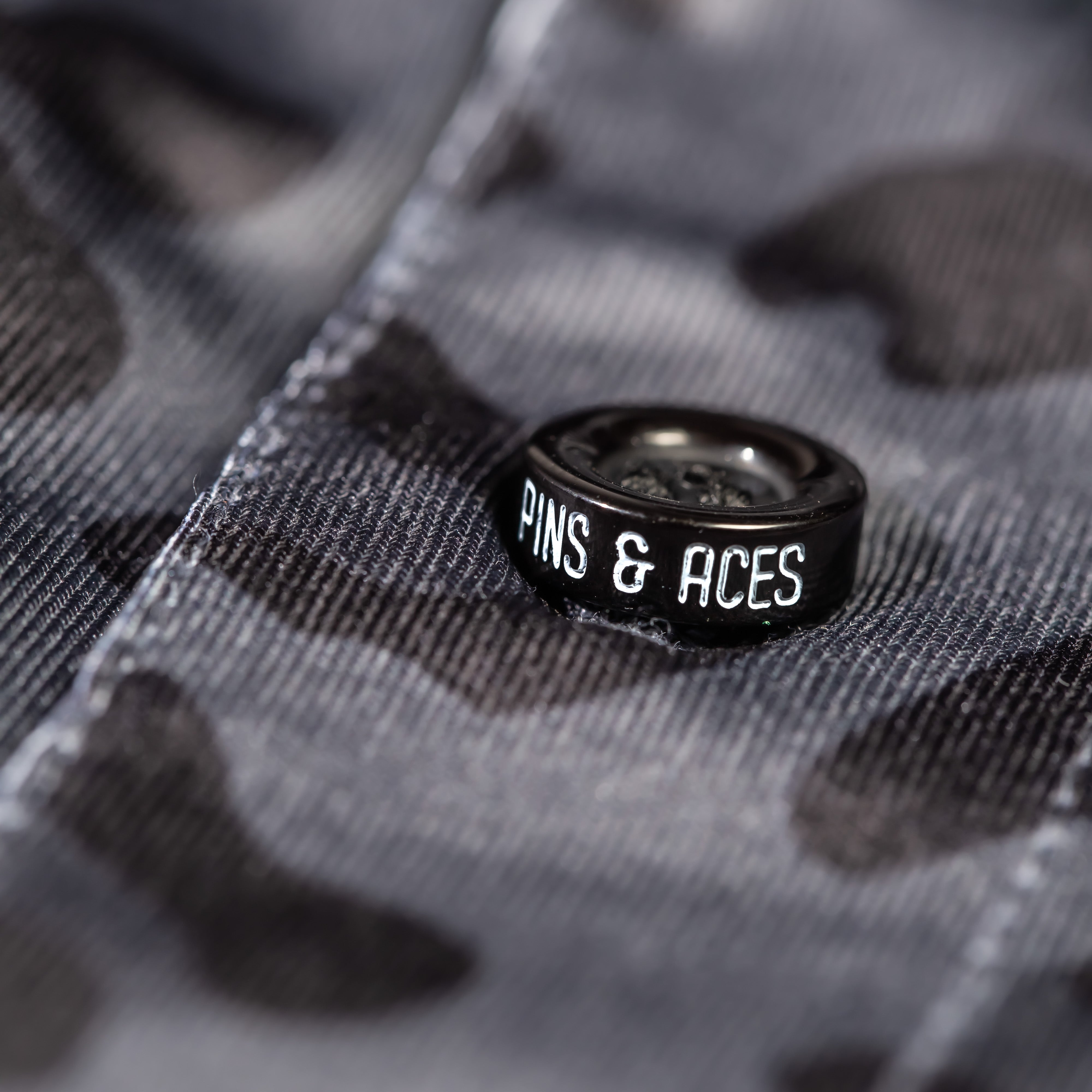 Close-up of a black jungle cat patterned fabric featuring a Pins & Aces logo button, showcasing bold golf apparel style.