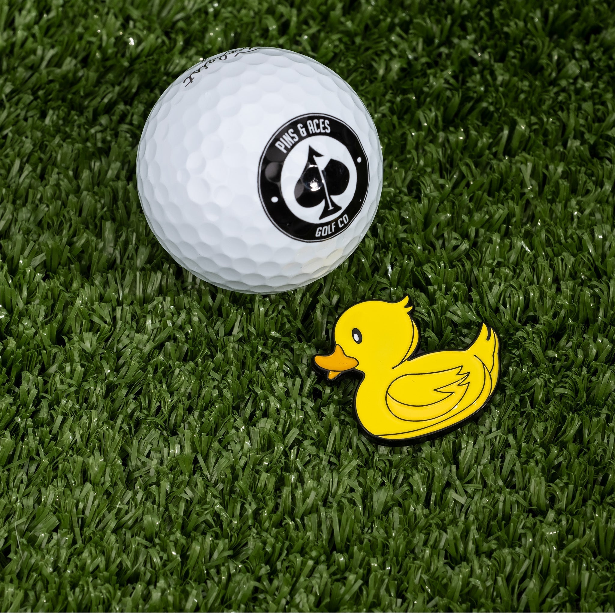 Bright yellow rubber ducky ball marker beside a golf ball on green turf, perfect for adding fun to your golf game.