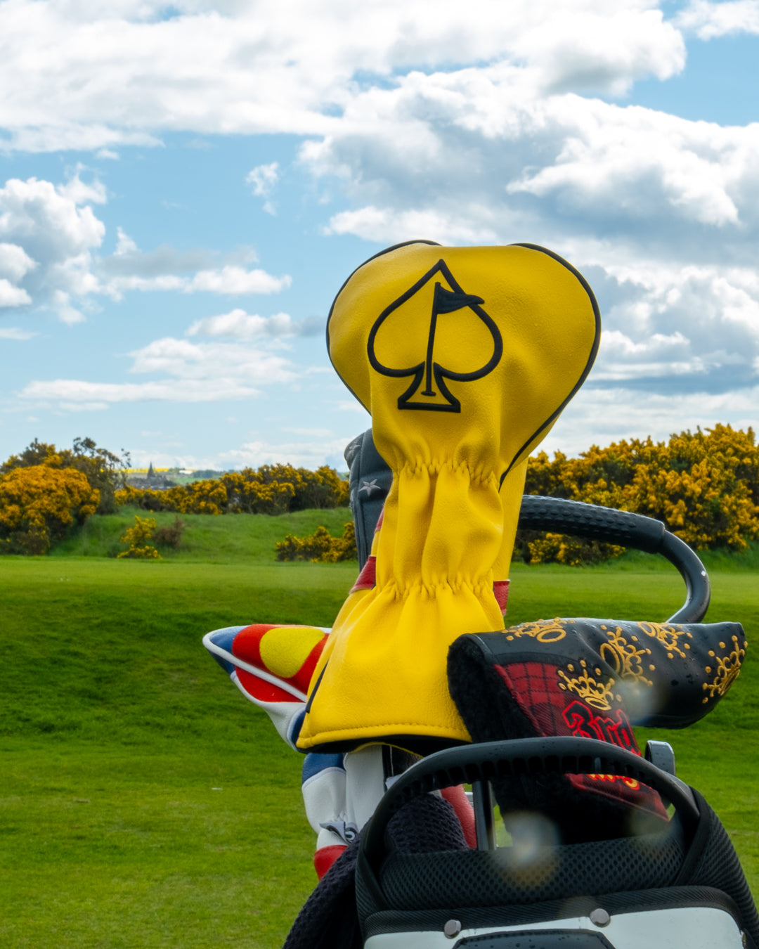 Bold yellow Scotland driver cover with a spade logo, set against a scenic golf course backdrop. Perfect for stylish golfers.