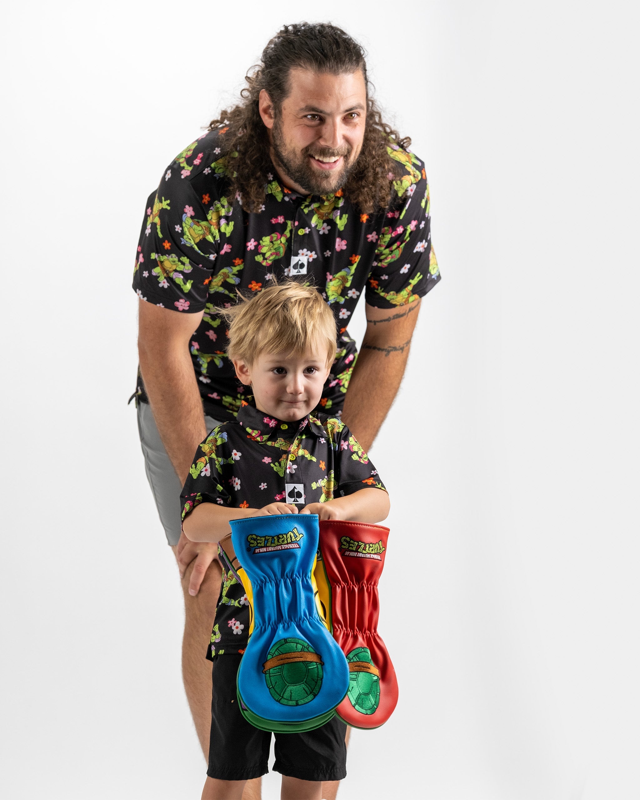 Father and son wear matching TMNT floral shirts, holding colorful turtle-themed gloves, showcasing fun family style.
