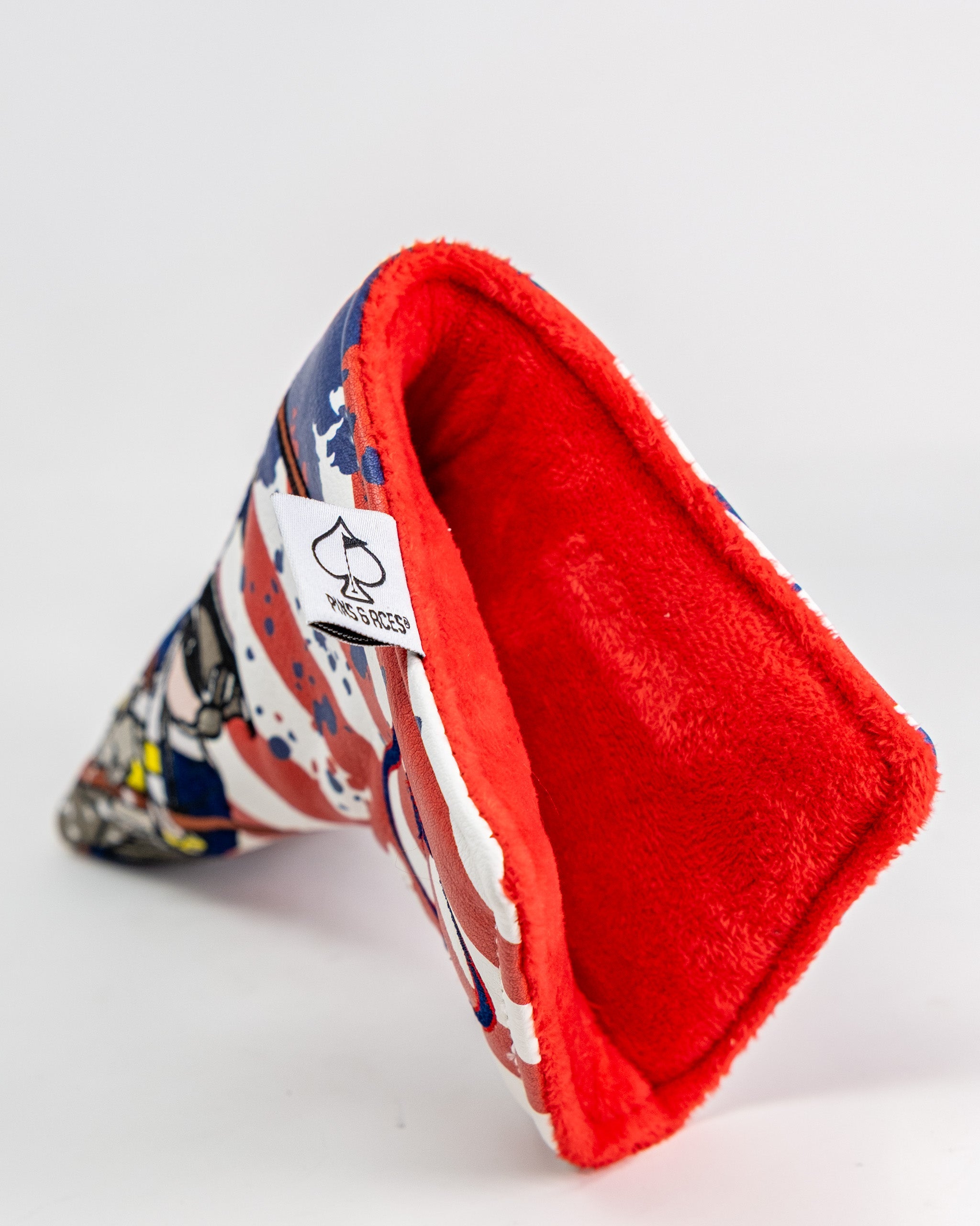 Colorful blade putter cover with a red plush interior and a white tag featuring a black spade logo.