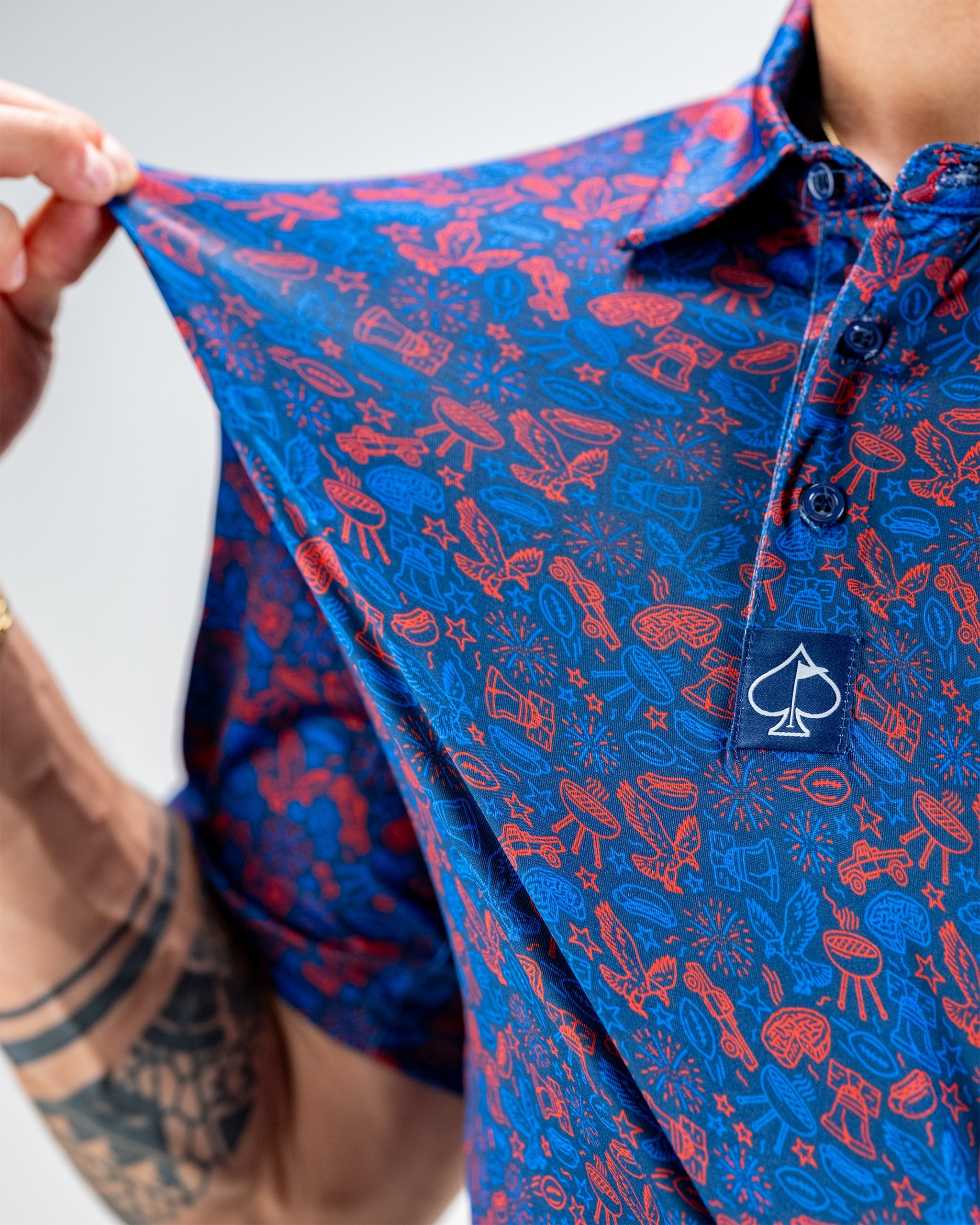 Navy polo shirt featuring a colorful doodle pattern of golf-related icons, held up to showcase its fabric and design.