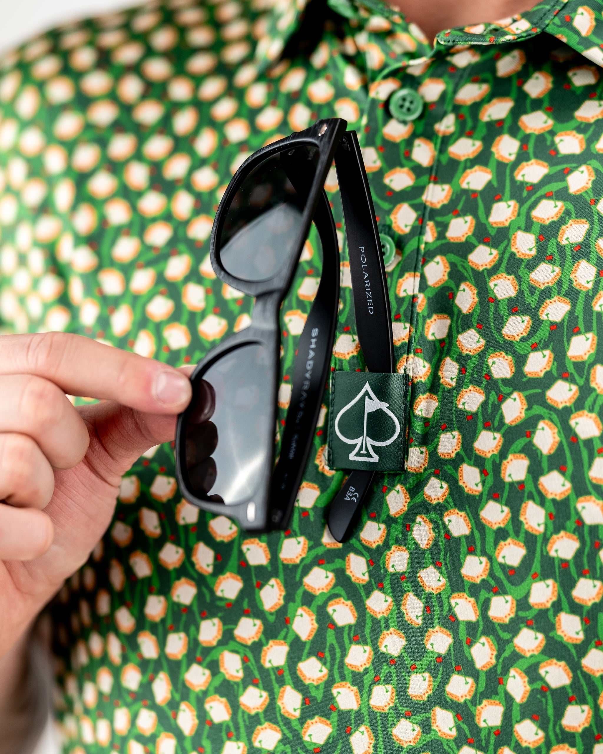 Bold black sunglasses with "POLARIZED" and "SHADYRAIN" on the arms, clipped to a green golf shirt with a white and orange ...