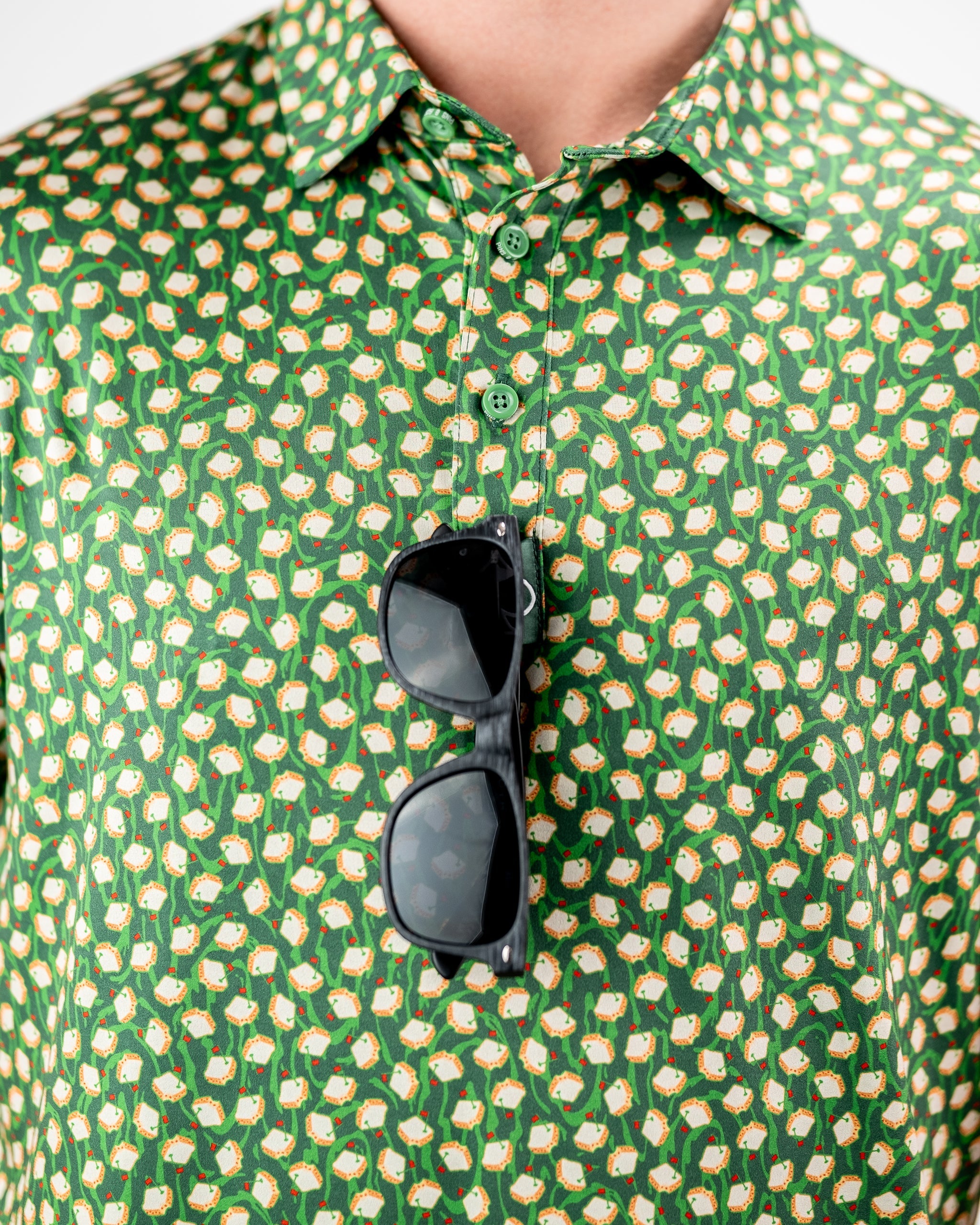 Close-up of a green golf shirt with a bold, repeating sushi roll pattern, featuring sunglasses hanging from the collar.