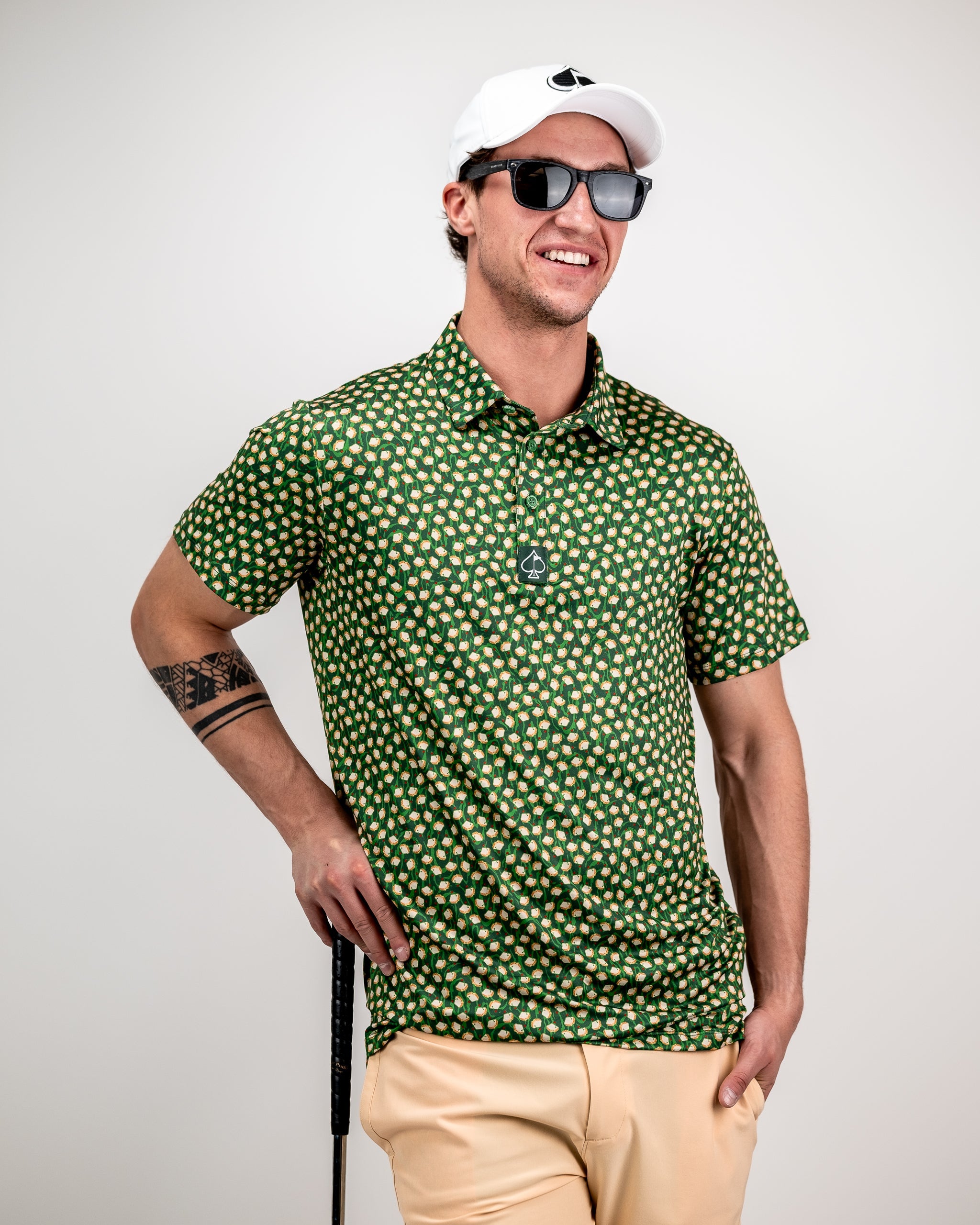 Man wearing a bold green golf shirt with a fun pattern, beige pants, black sunglasses, and a white cap for standout golf s...